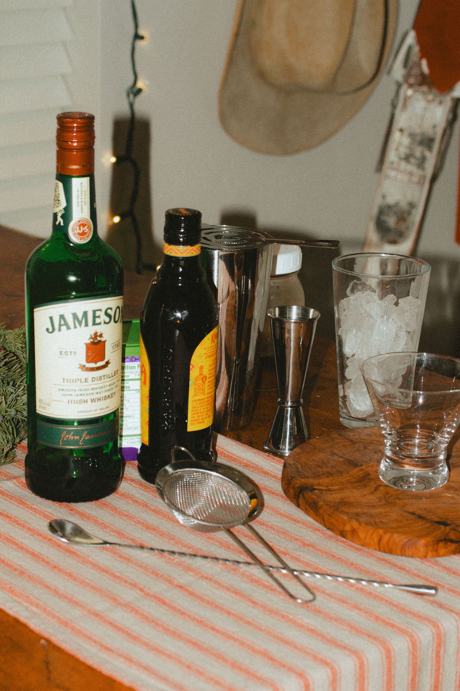 Bottles of Jameson whiskey and other liquors arranged on a striped tablecloth with drinking glasses and utensils fro cocktails in the making