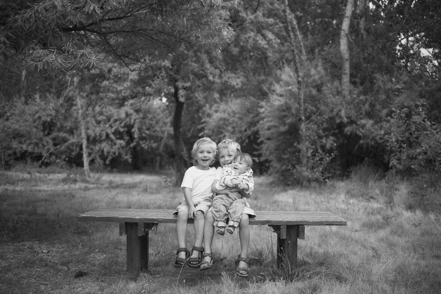 Black and white portrait of two young siblings sitting together on an outdoor bench.