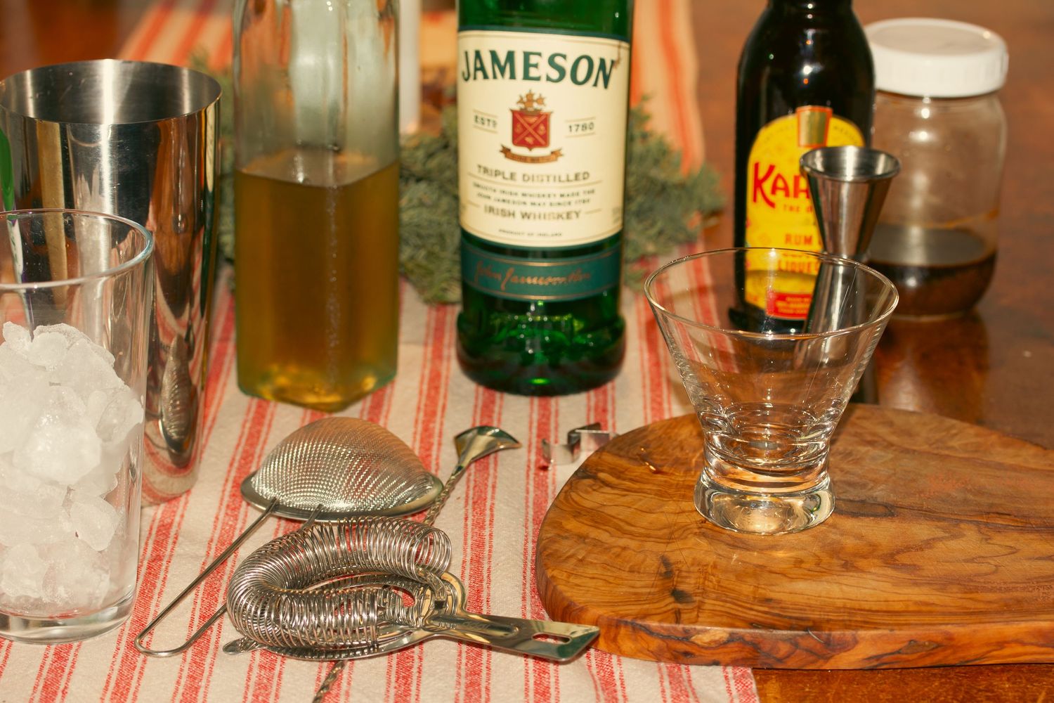 Various liquor bottles and glasses lined up on a wooden bar counter in dim lighting styled by stoked media