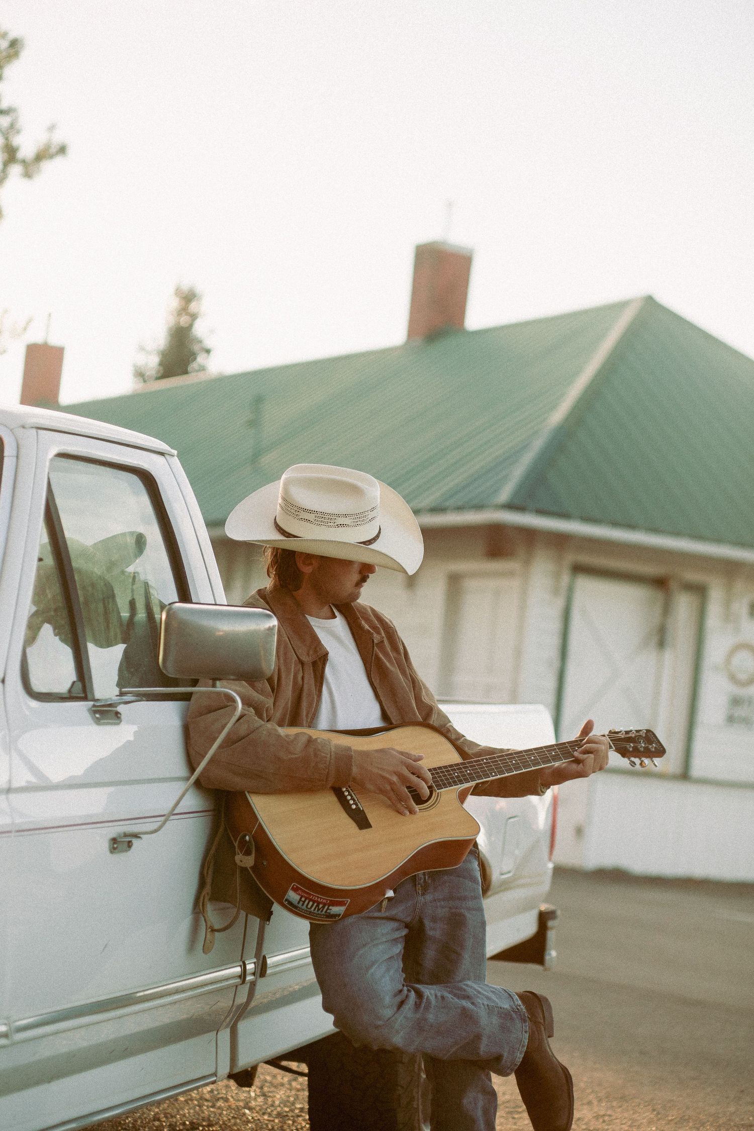 Guitarist leans on his truck in the blissful summer sun in this film style photo showcasing him playing music by a train depo in Idaho