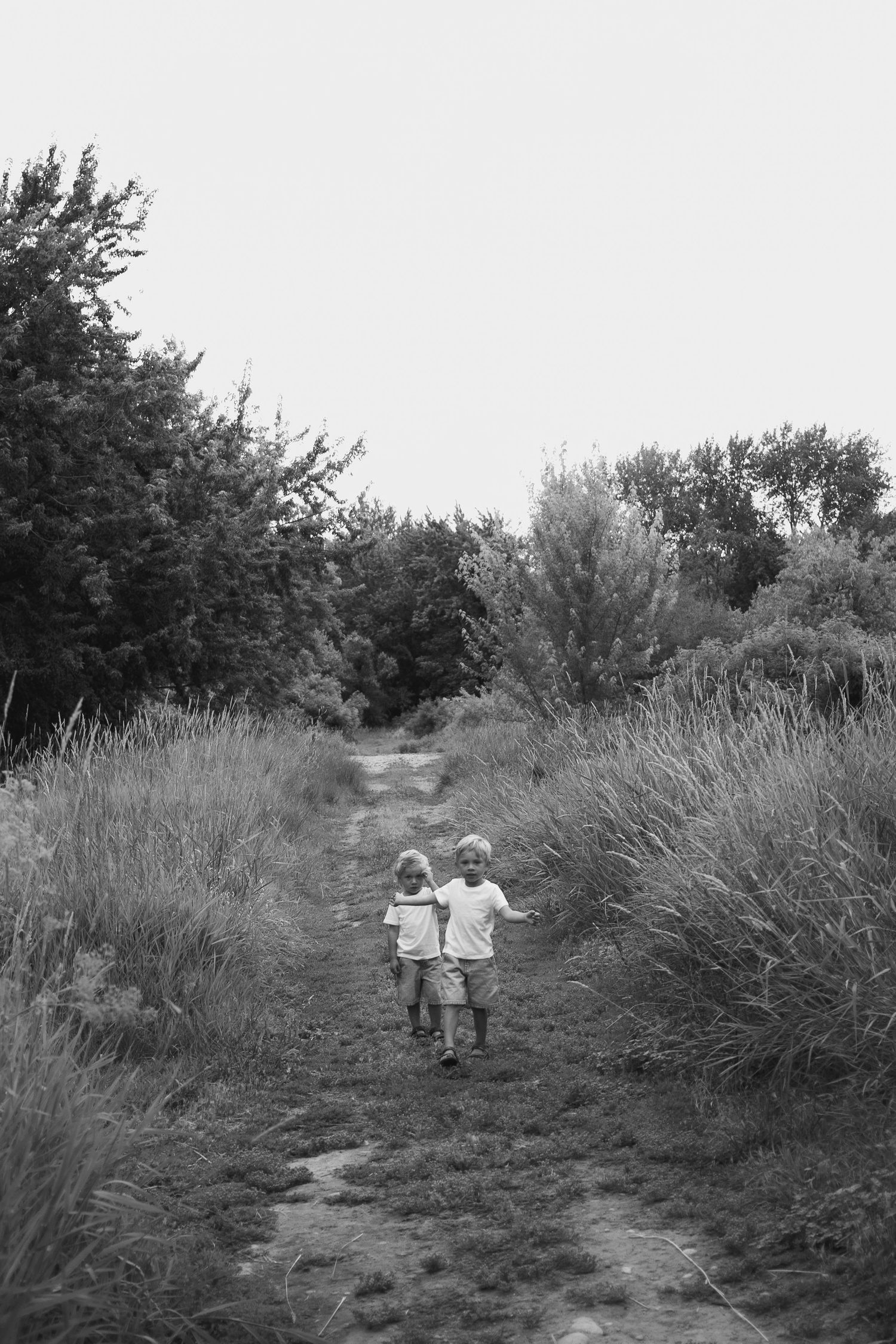 Black and white photo of two young children walking hand in hand down a rural path.