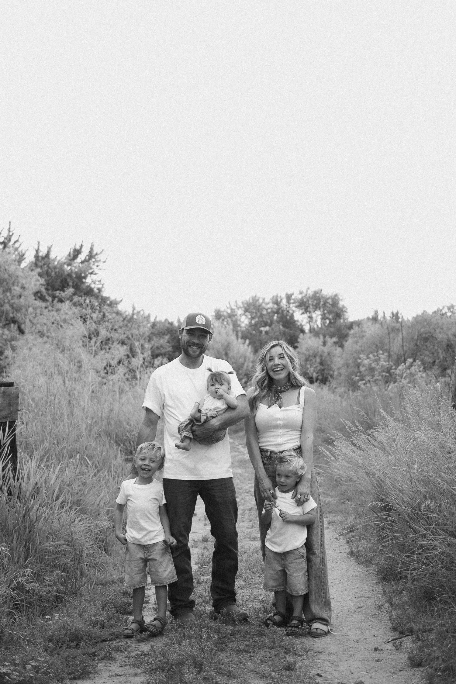 Black and white family portrait of parents with three young children on a nature path.