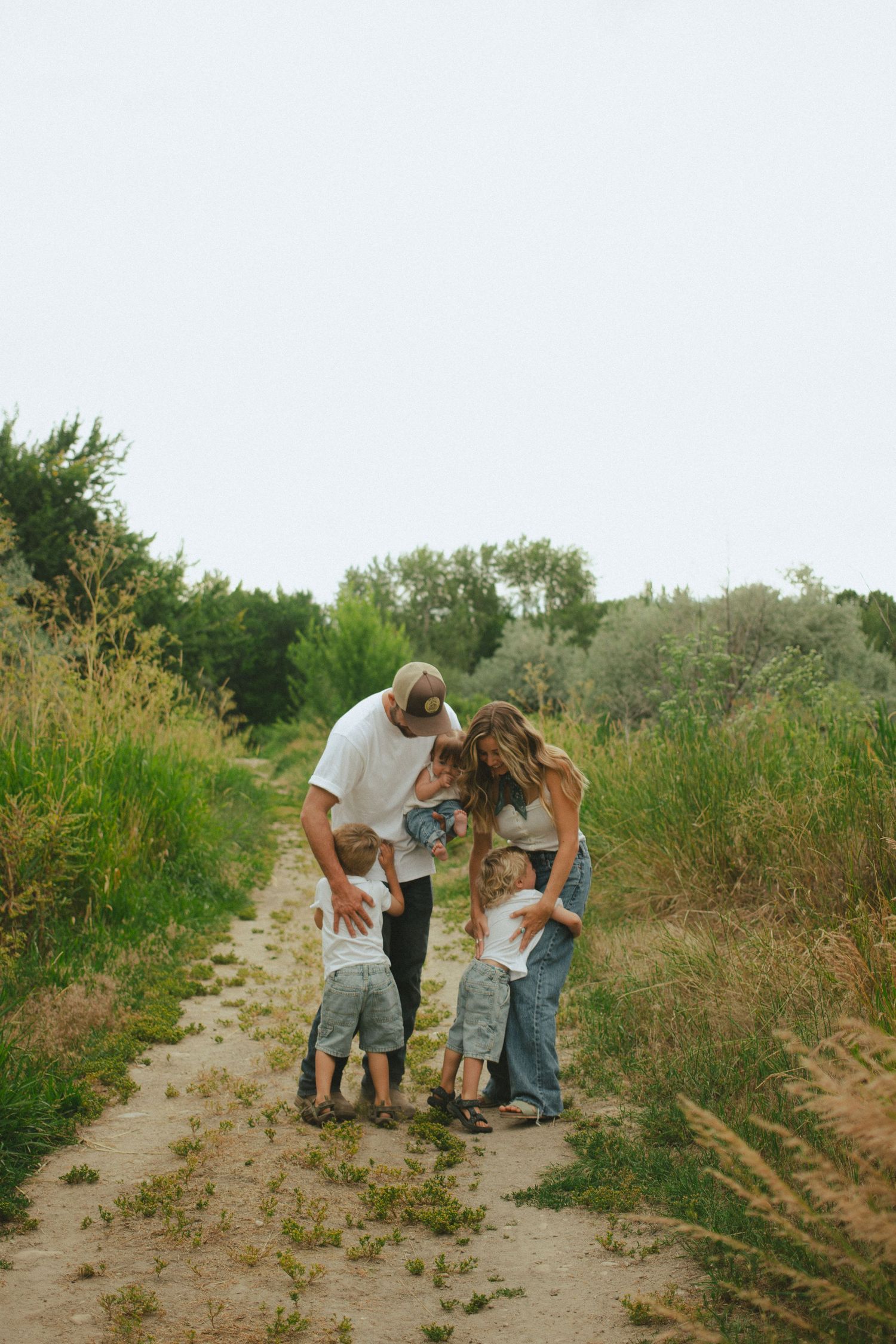 Family of five shares a warm group hug on a rustic dirt path outdoors.