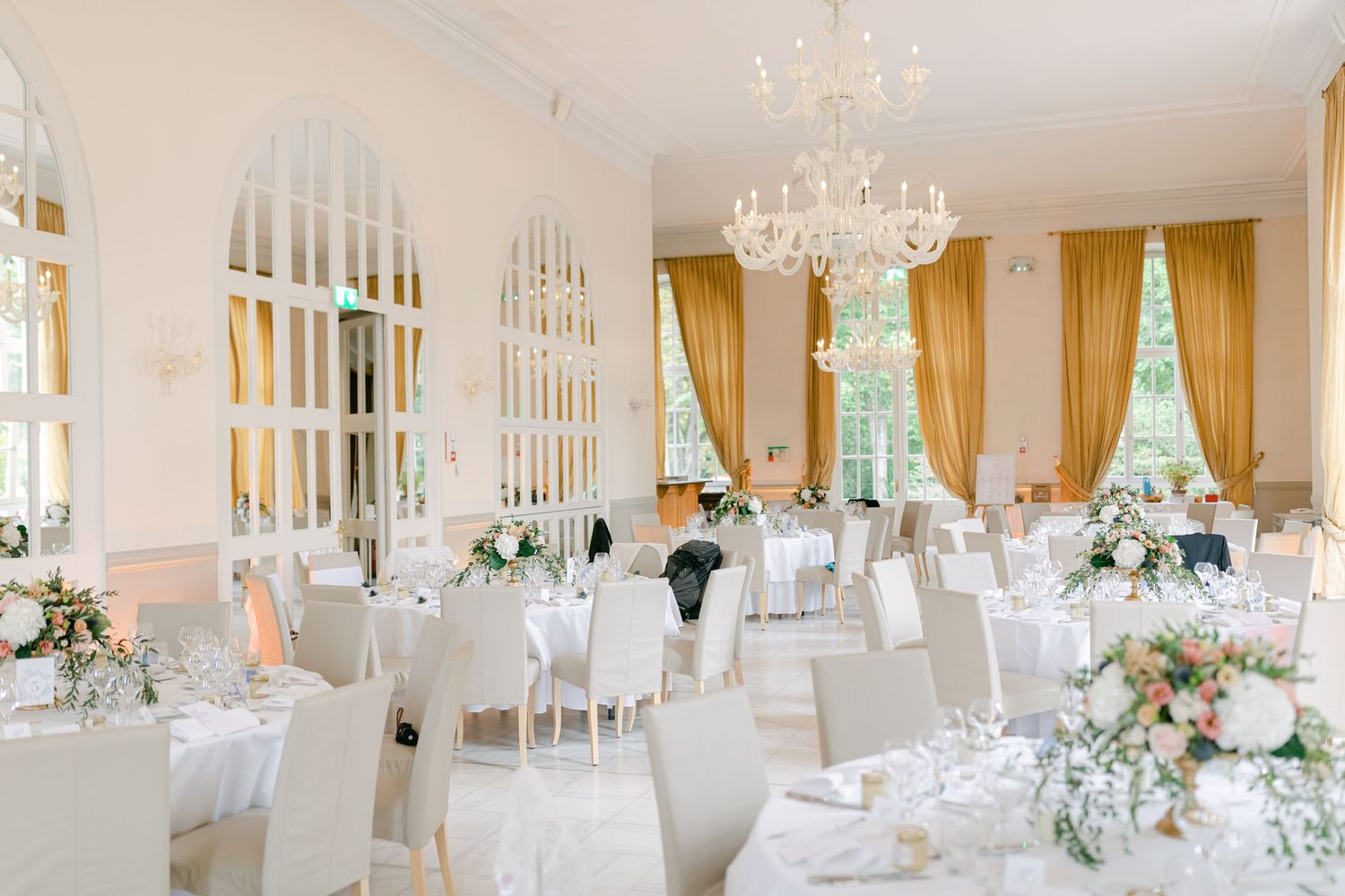 Bright white wedding reception venue with crystal chandeliers and elegant table settings.