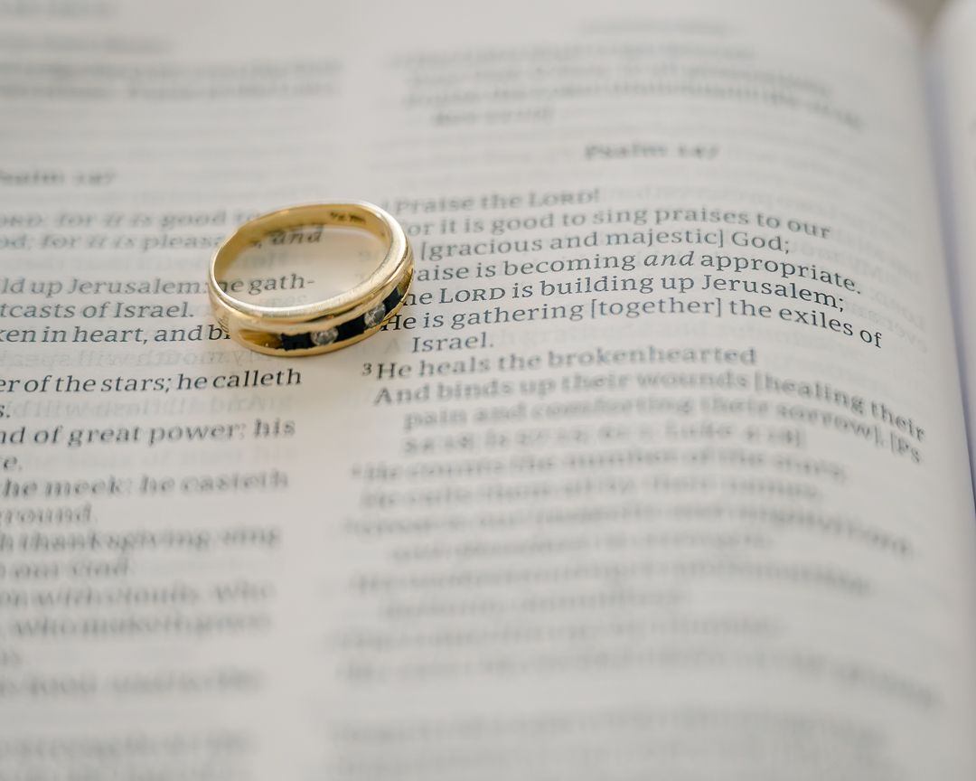 A golden wedding ring placed on an open Bible page.