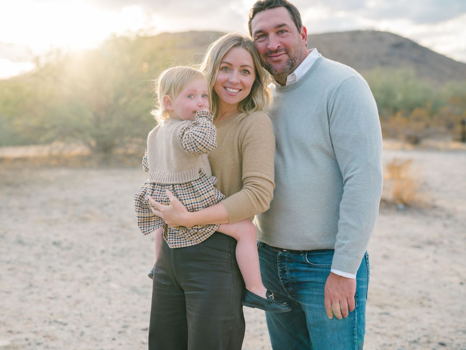 Family portrait in casual sweaters against desert mountain backdrop at sunset.