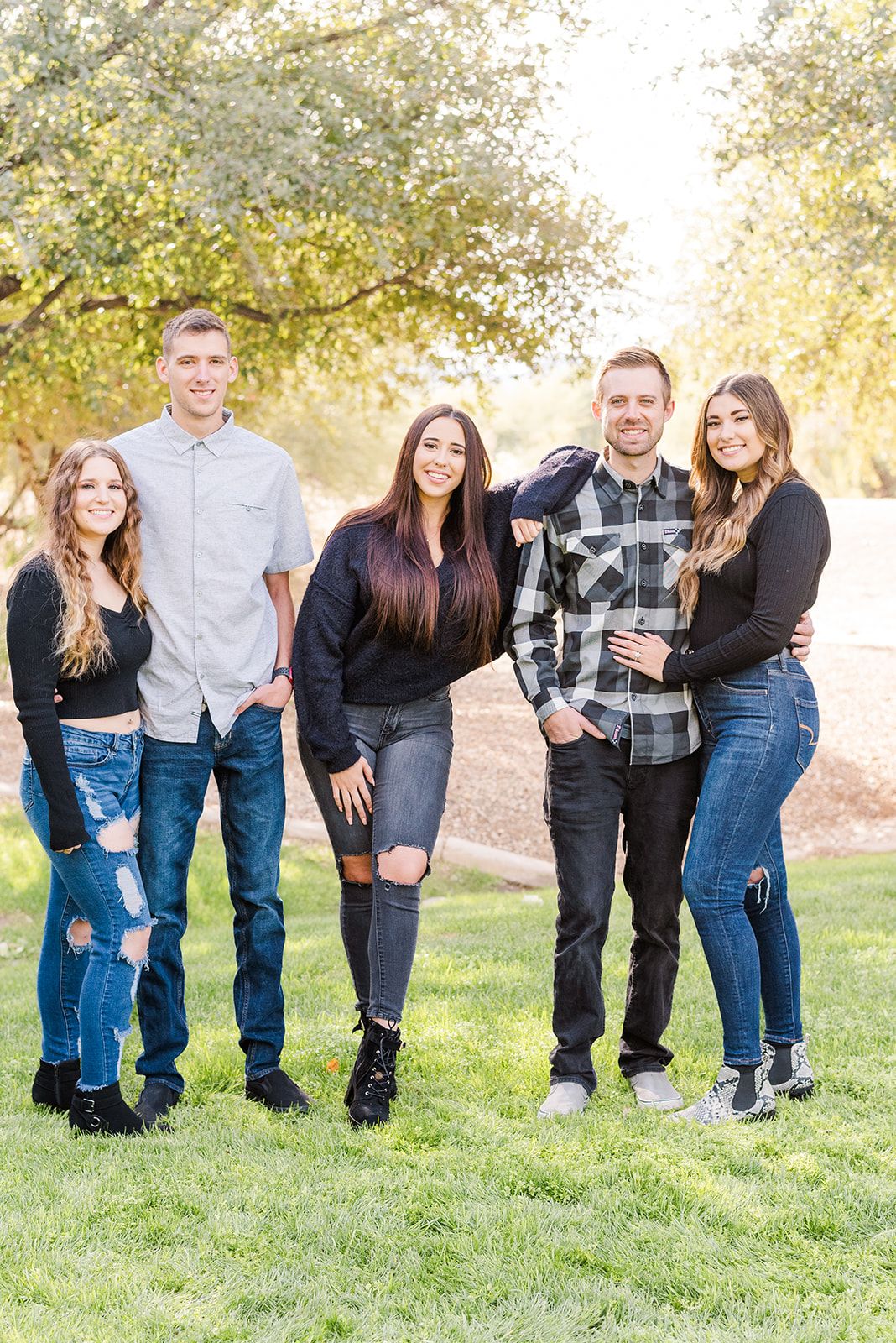 A group in casual attire poses together on grass with trees in the background during golden hour.