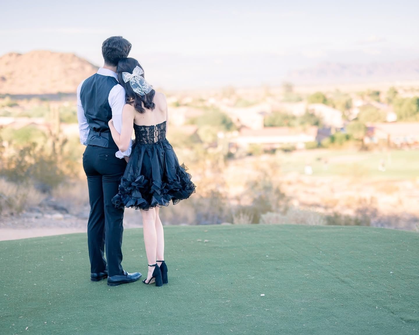 A couple shares an intimate moment while standing on a golf course overlooking a desert landscape.