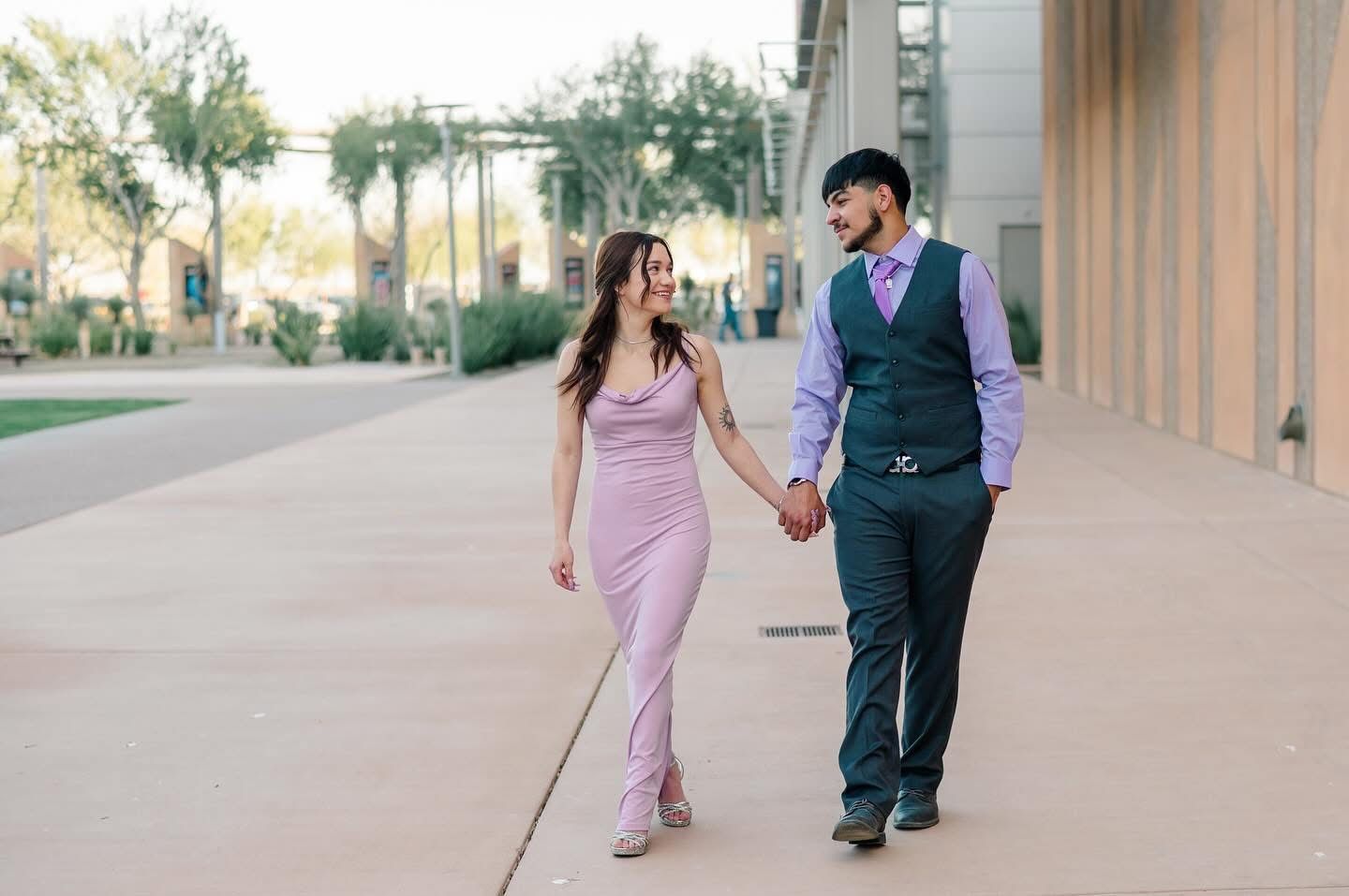 Couple walking hand in hand along a pathway, dressed in purple and formal attire.