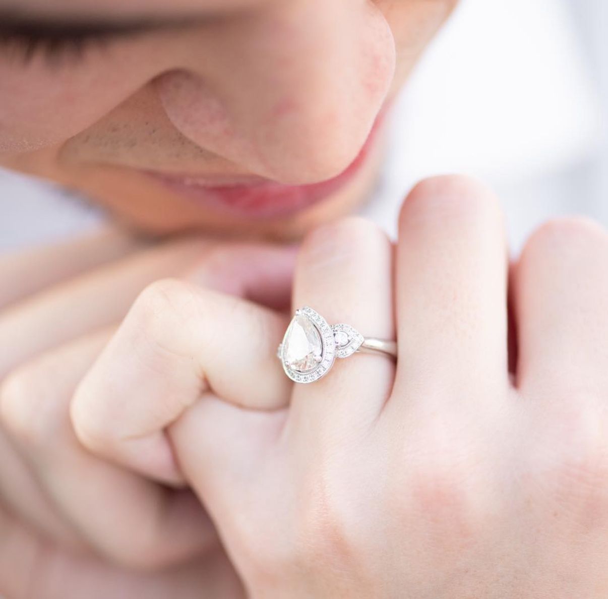 Close-up of a delicate silver engagement ring worn on a hand against a soft background.