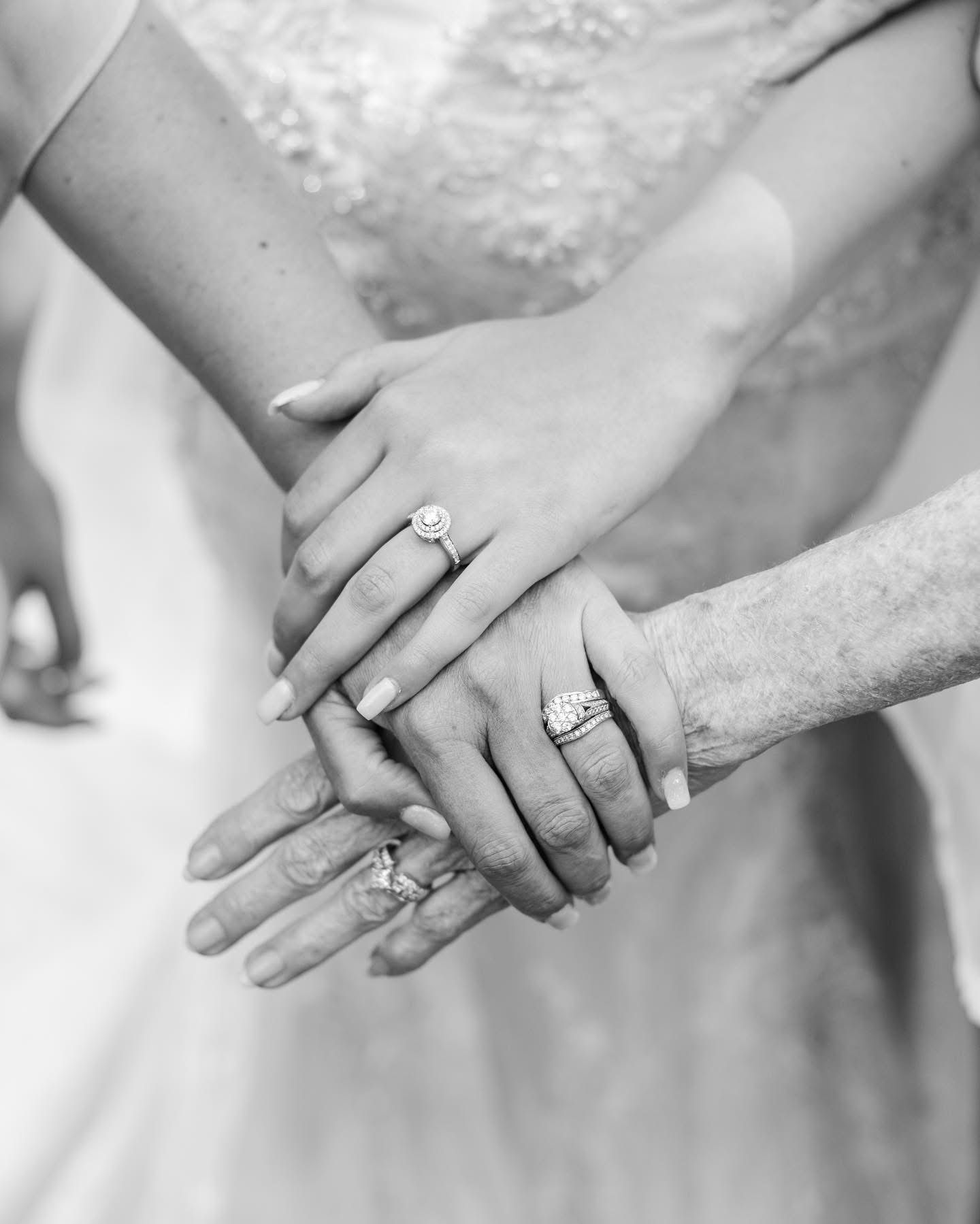 Black and white close-up of hands stacked together showing wedding rings.