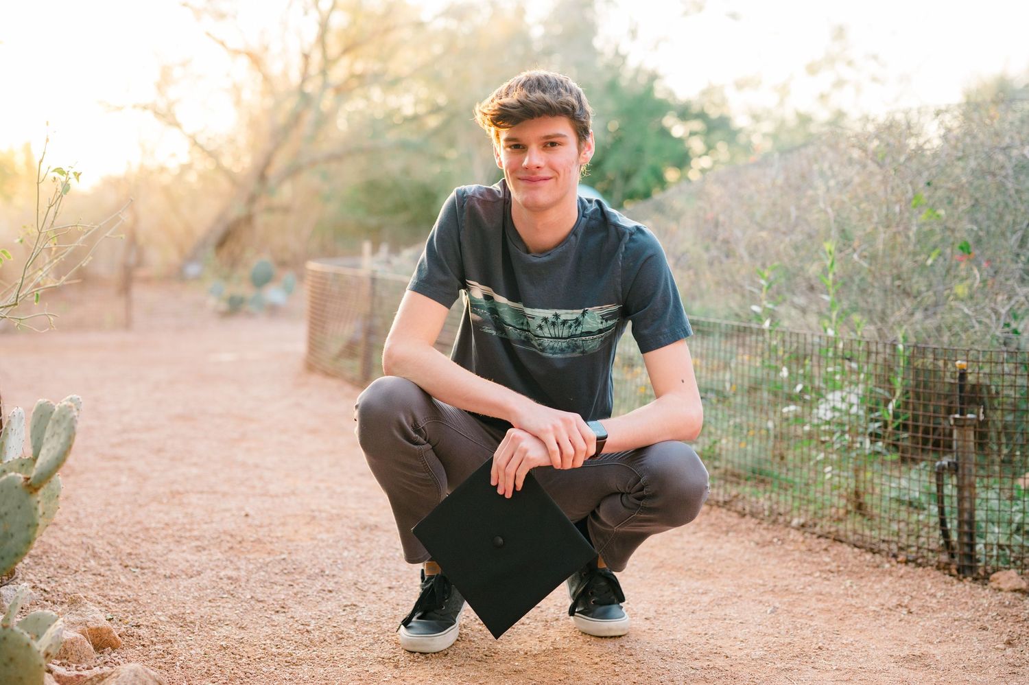 Casual portrait of someone crouching on a desert path during golden hour.