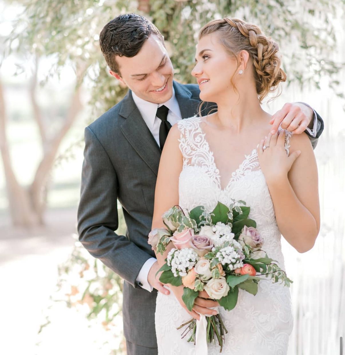 Romantic wedding portrait showing couple with pink and white floral bouquet outdoors.