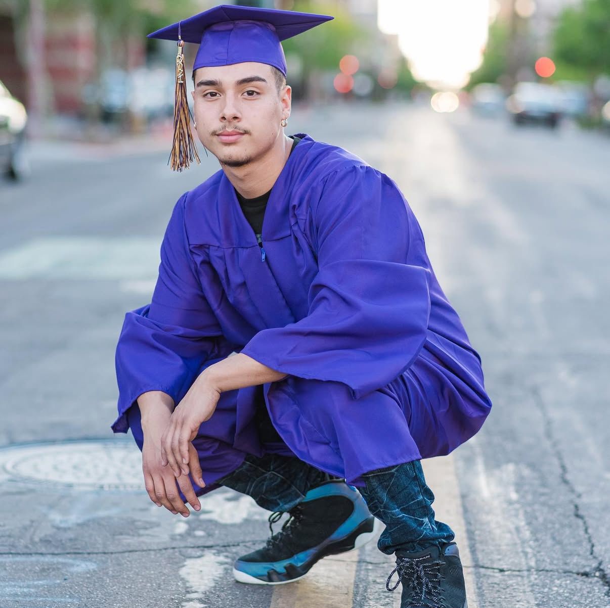 Graduate in royal blue cap and gown crouches on street for graduation photo.
