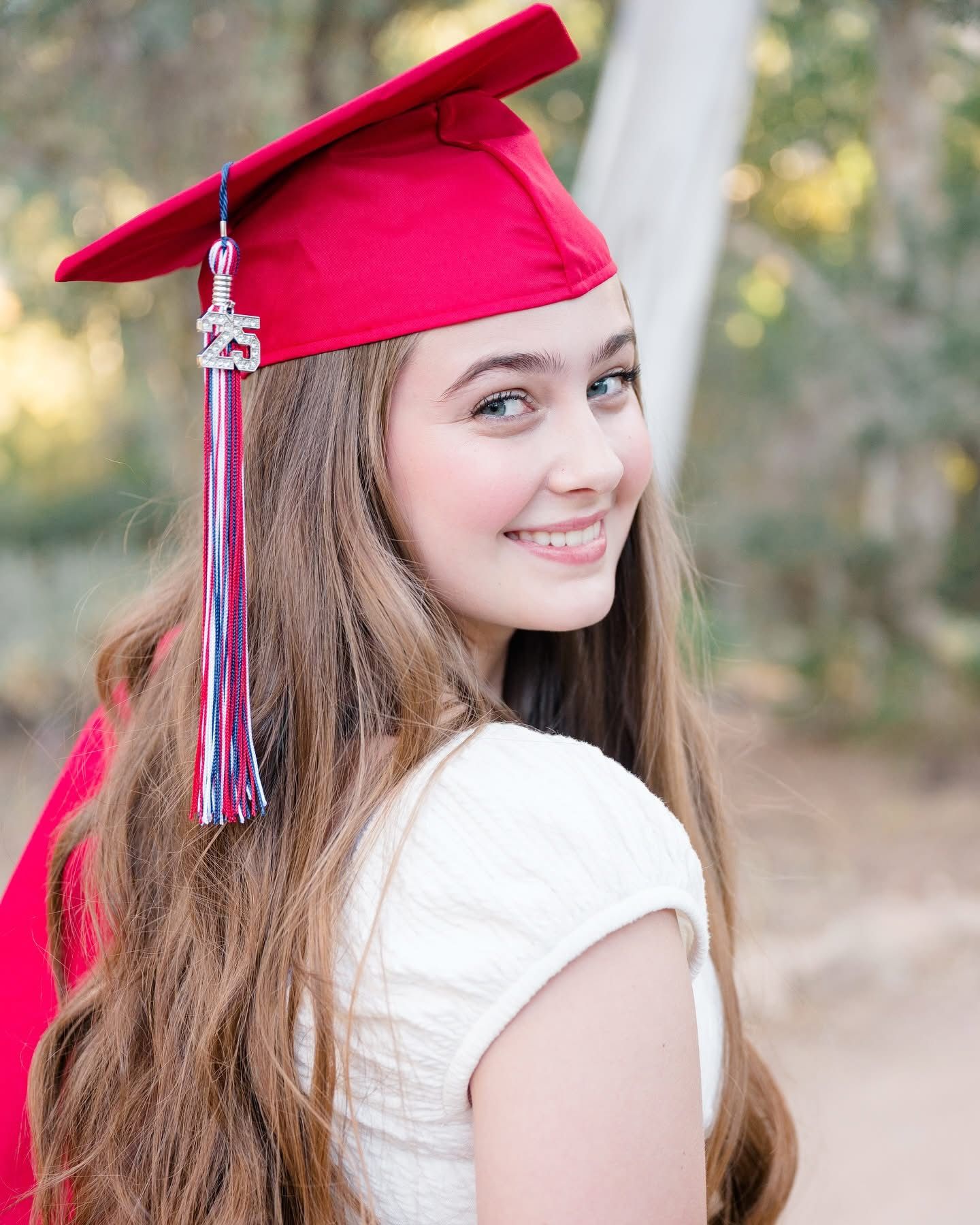 Graduate in red cap and gown with tassel smiling against natural background.