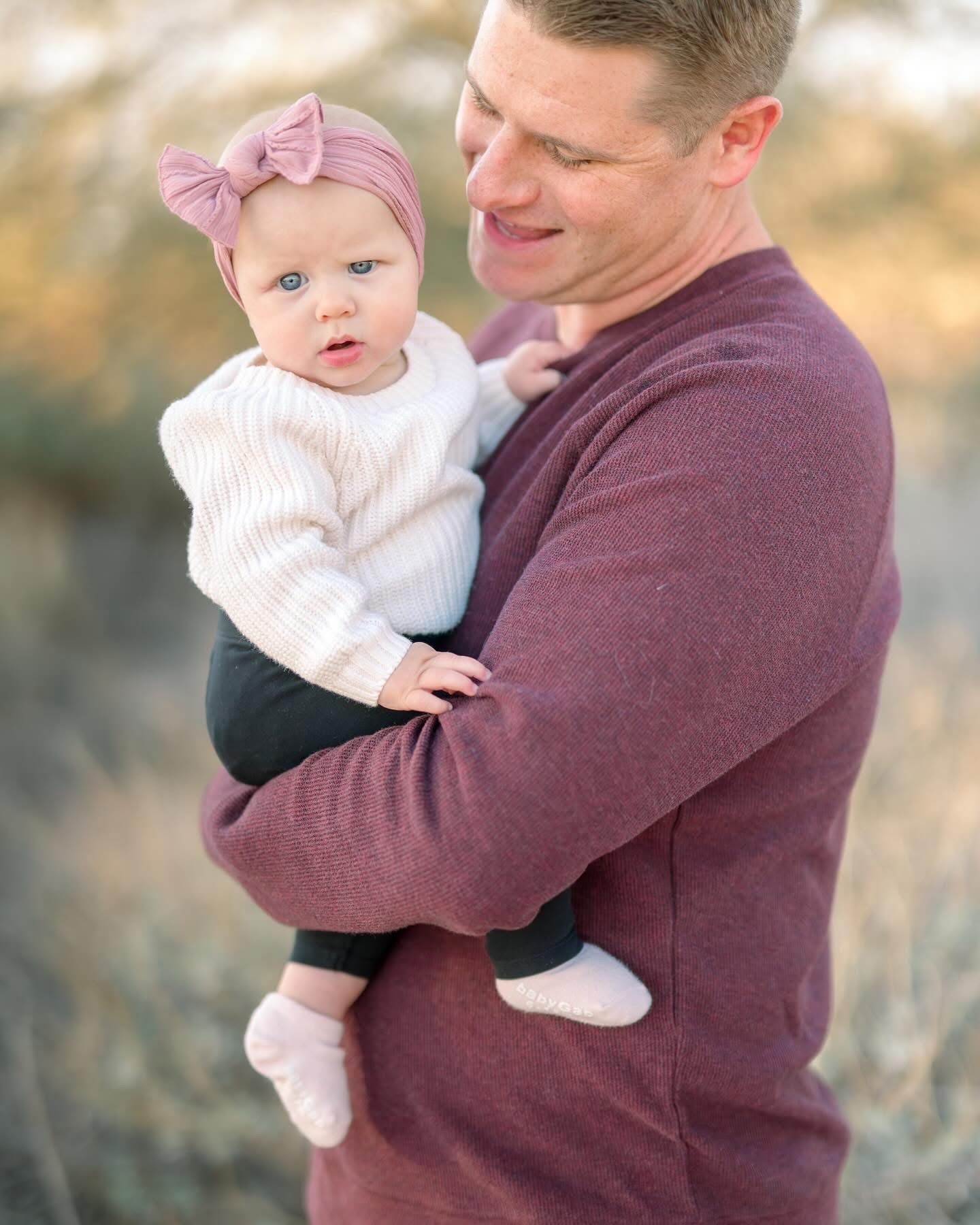 Sweet moment with baby wearing white sweater and pink bow captured in natural setting.