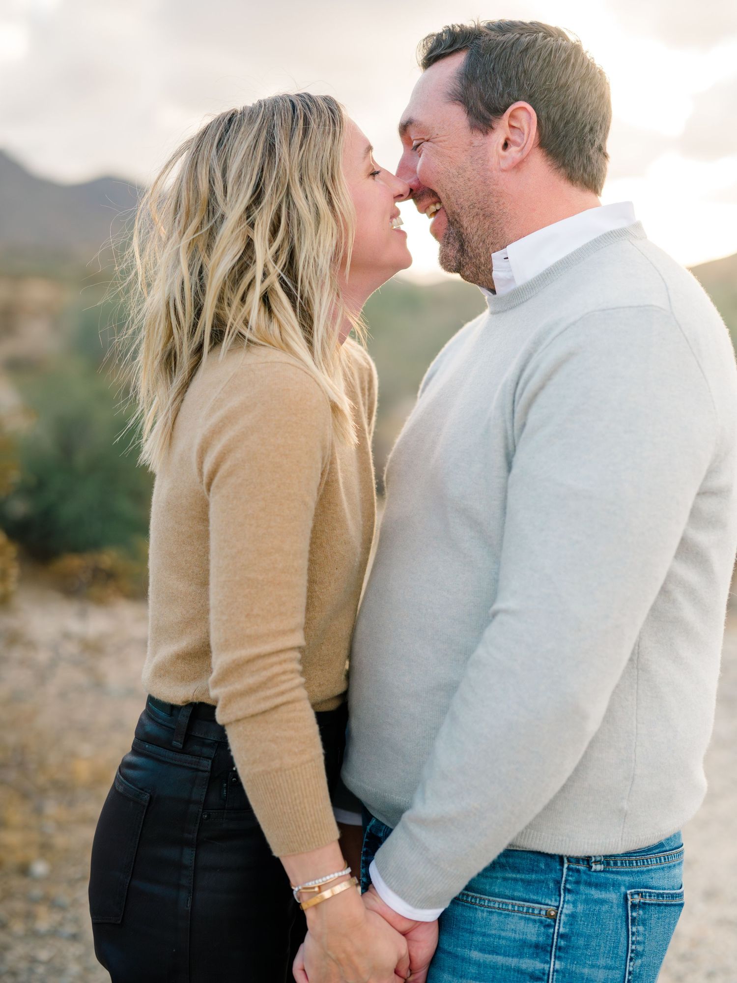 Intimate couple's portrait in matching sweaters against desert landscape at sunset.