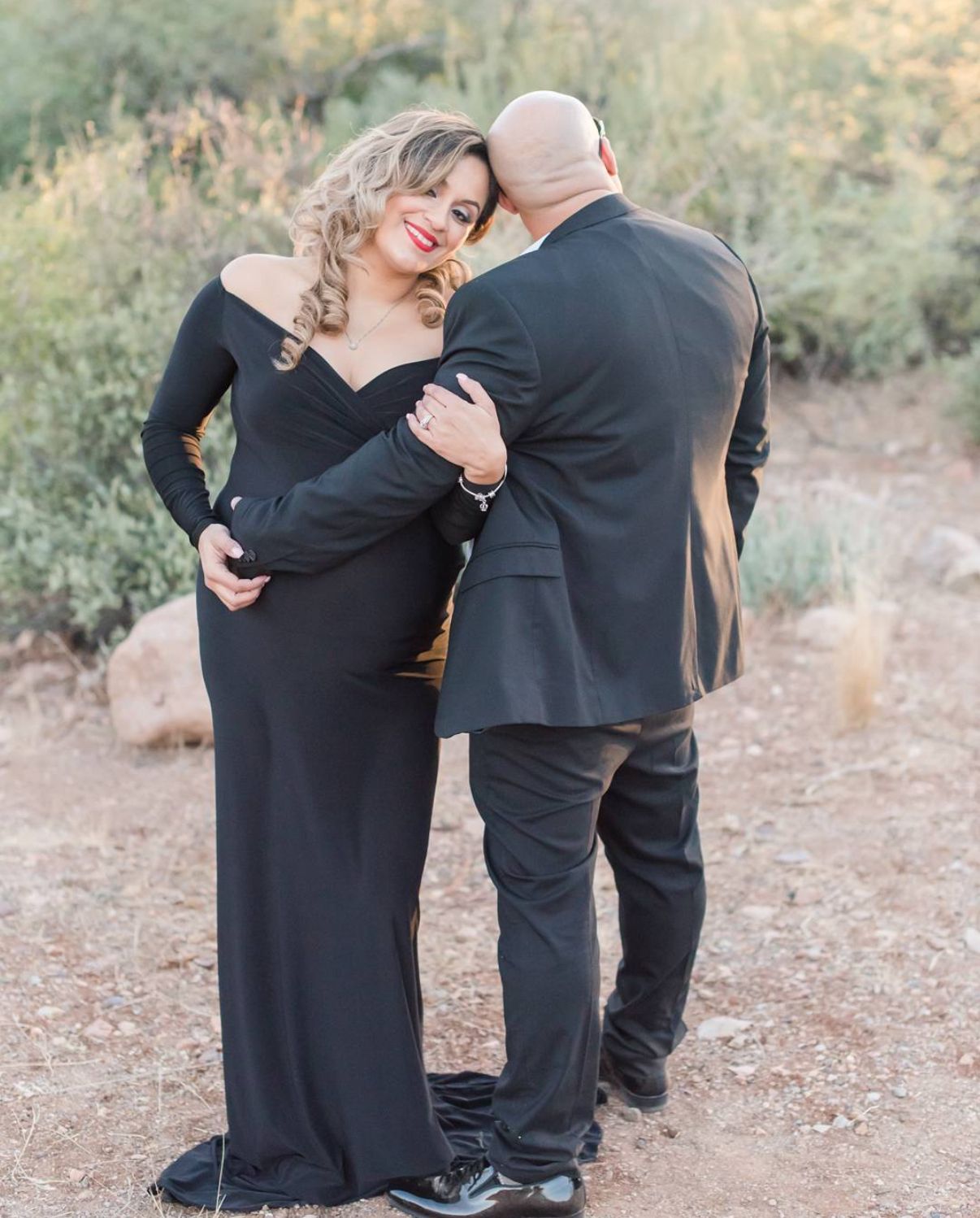 Intimate maternity portrait of couple in formal attire embracing in outdoor setting.
