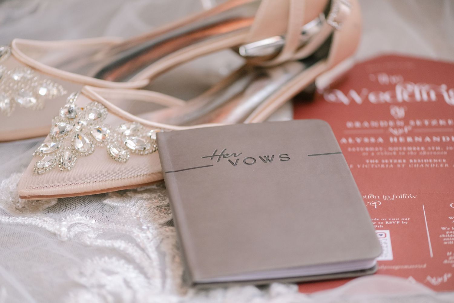A wedding vow book alongside elegant pink bridal shoes with crystal embellishments.