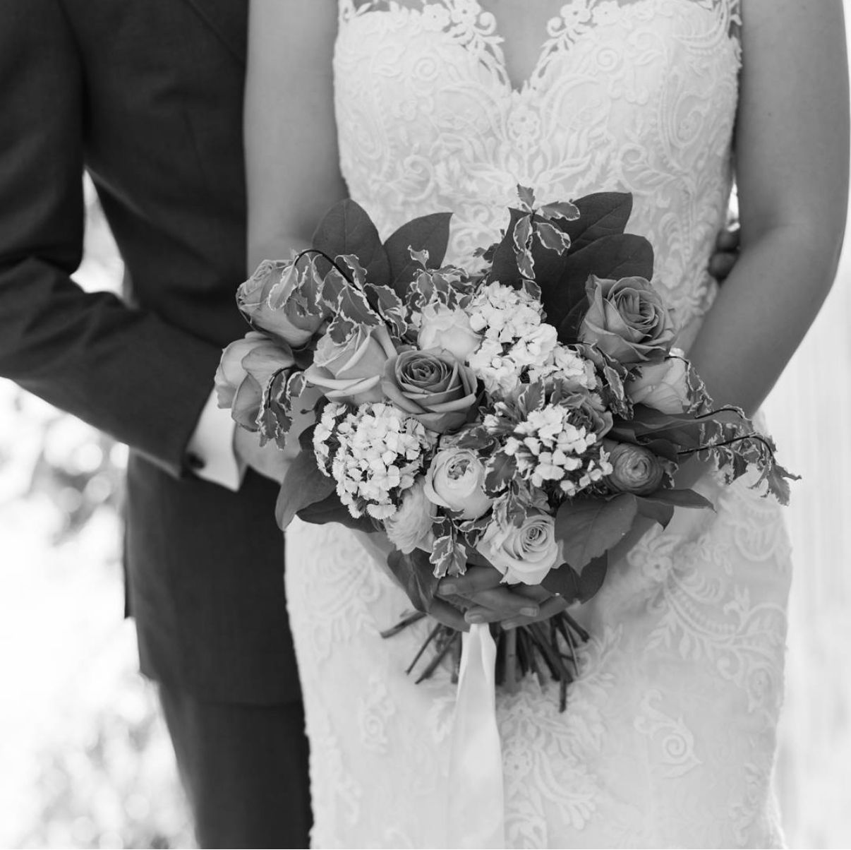 Black and white detail of wedding dress and bouquet with roses and mixed flowers.
