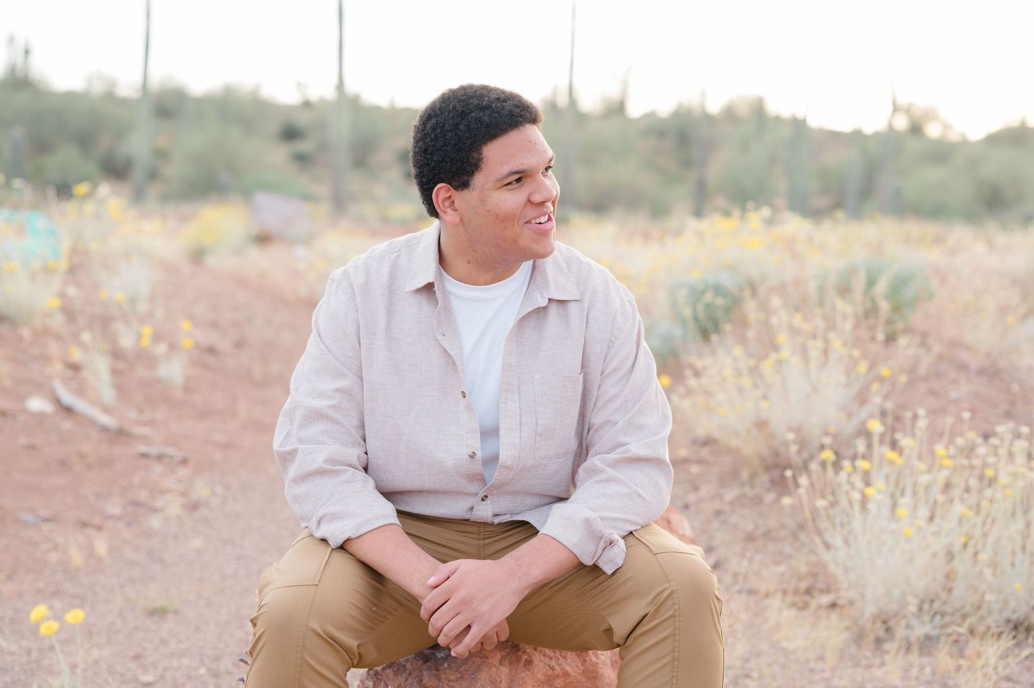 Person sits outdoors in a desert setting wearing casual attire against a natural backdrop.