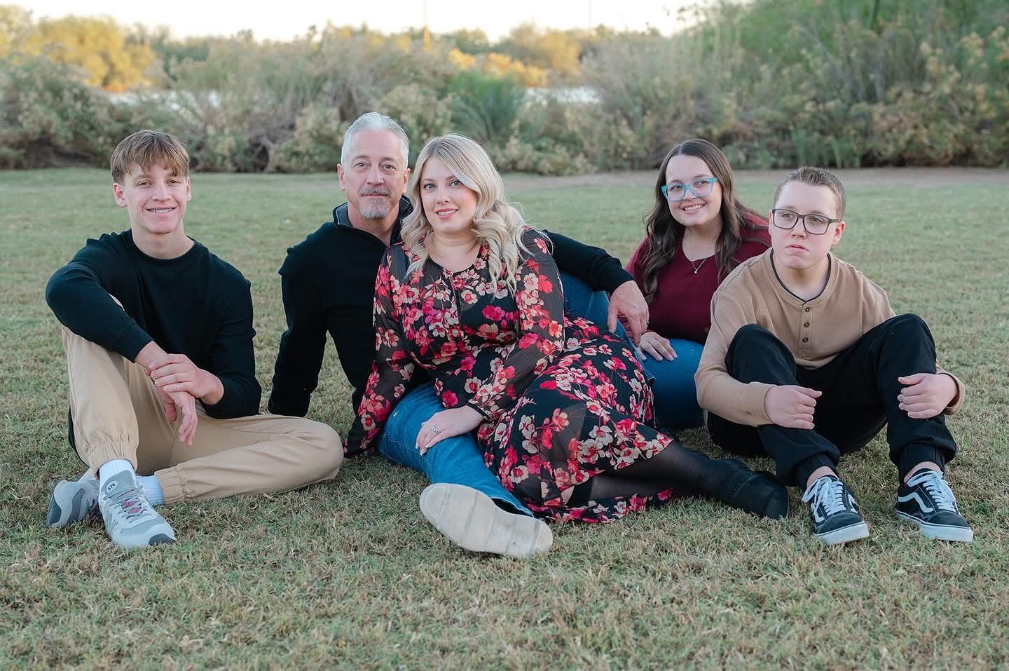 Group photo of five people sitting casually on grass at sunset.