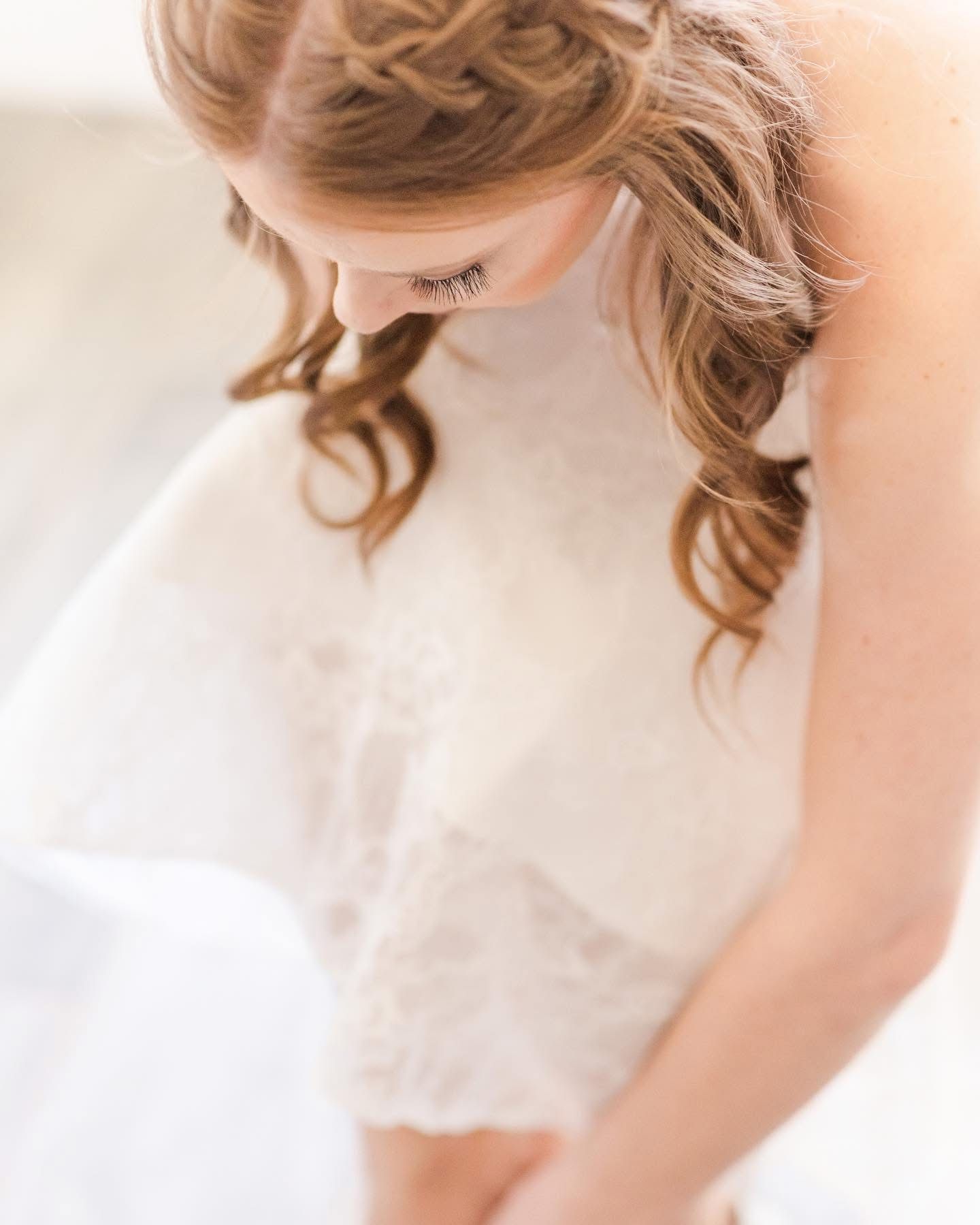Close-up of delicate lace details on white bridal gown with soft curled hair.