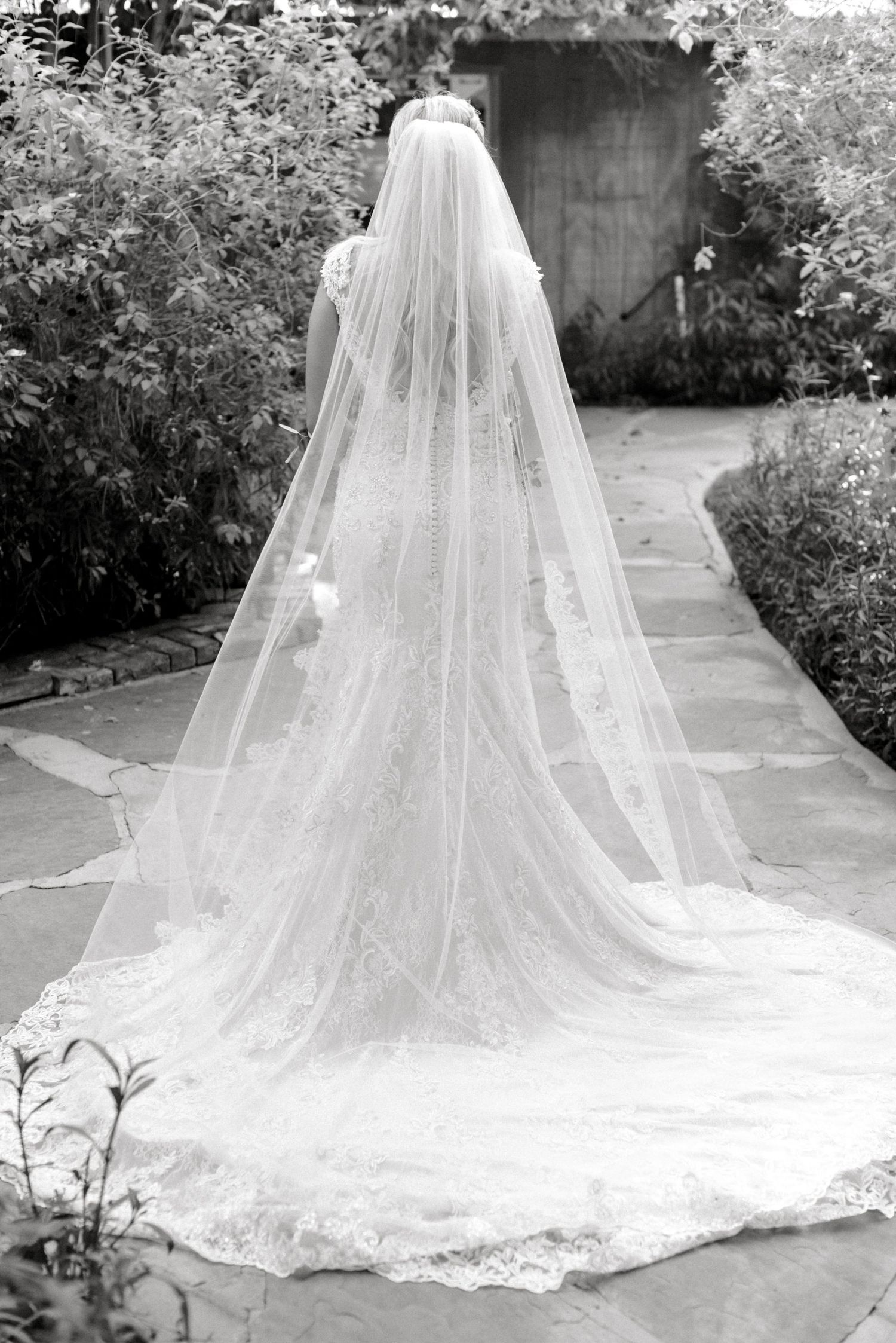 Black and white photo of a dramatic cathedral length wedding veil on stone pathway.