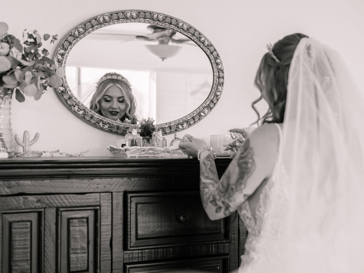 A vintage-style black and white photograph of a bride looking in an ornate mirror.
