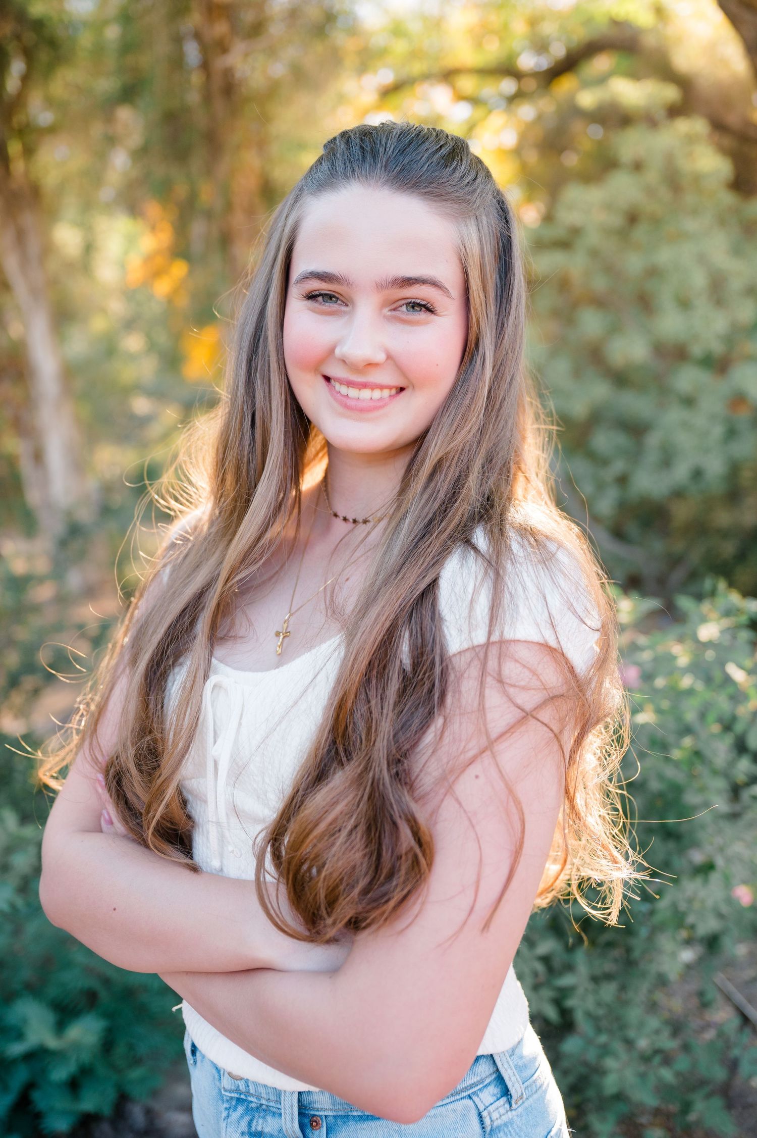 Natural outdoor portrait with long hair and white top against green foliage background.