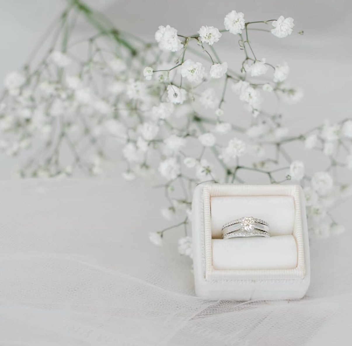 Engagement ring in white velvet box with delicate baby's breath flowers above.