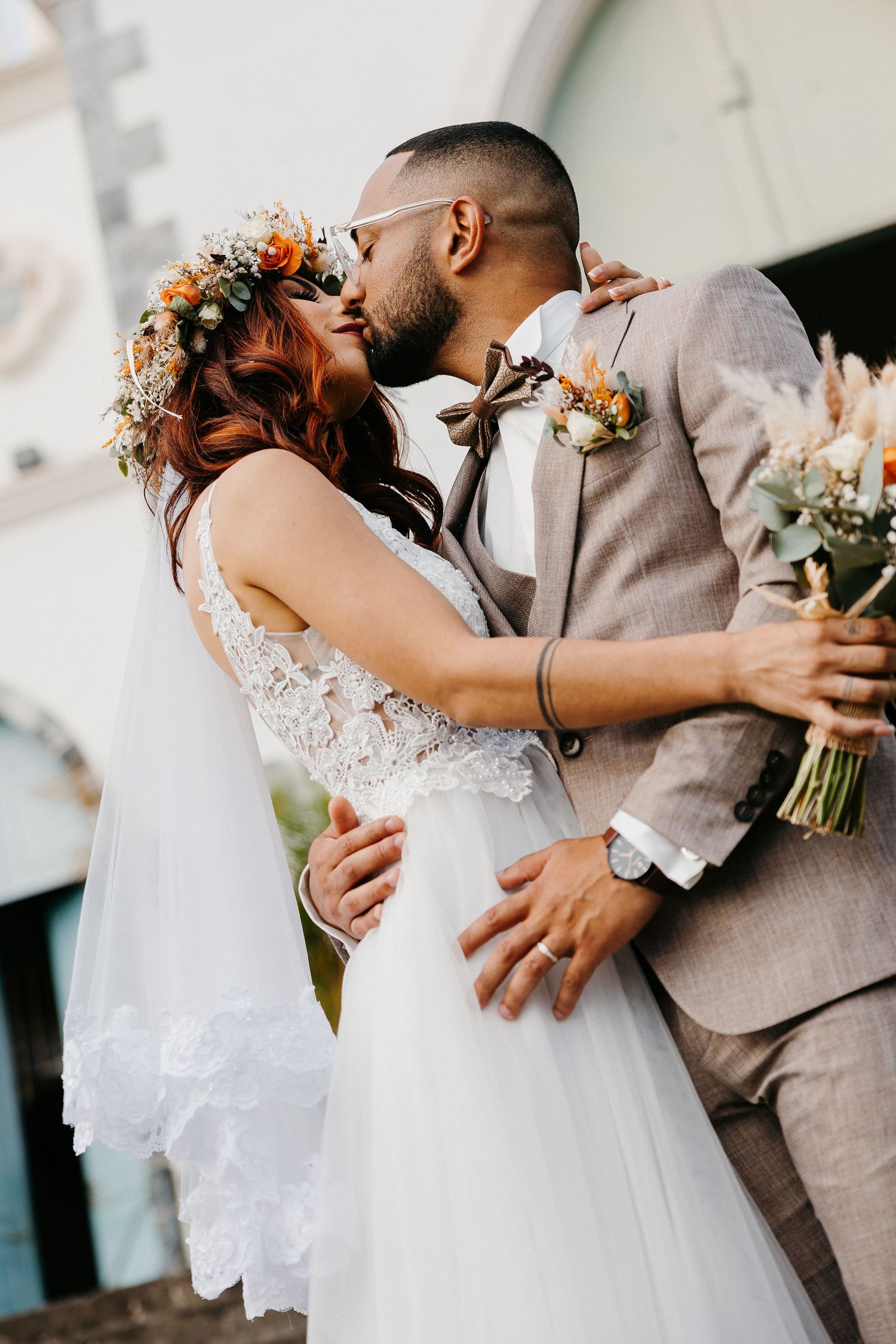A romantic wedding kiss captured between newlyweds with floral bouquet and decorative details.