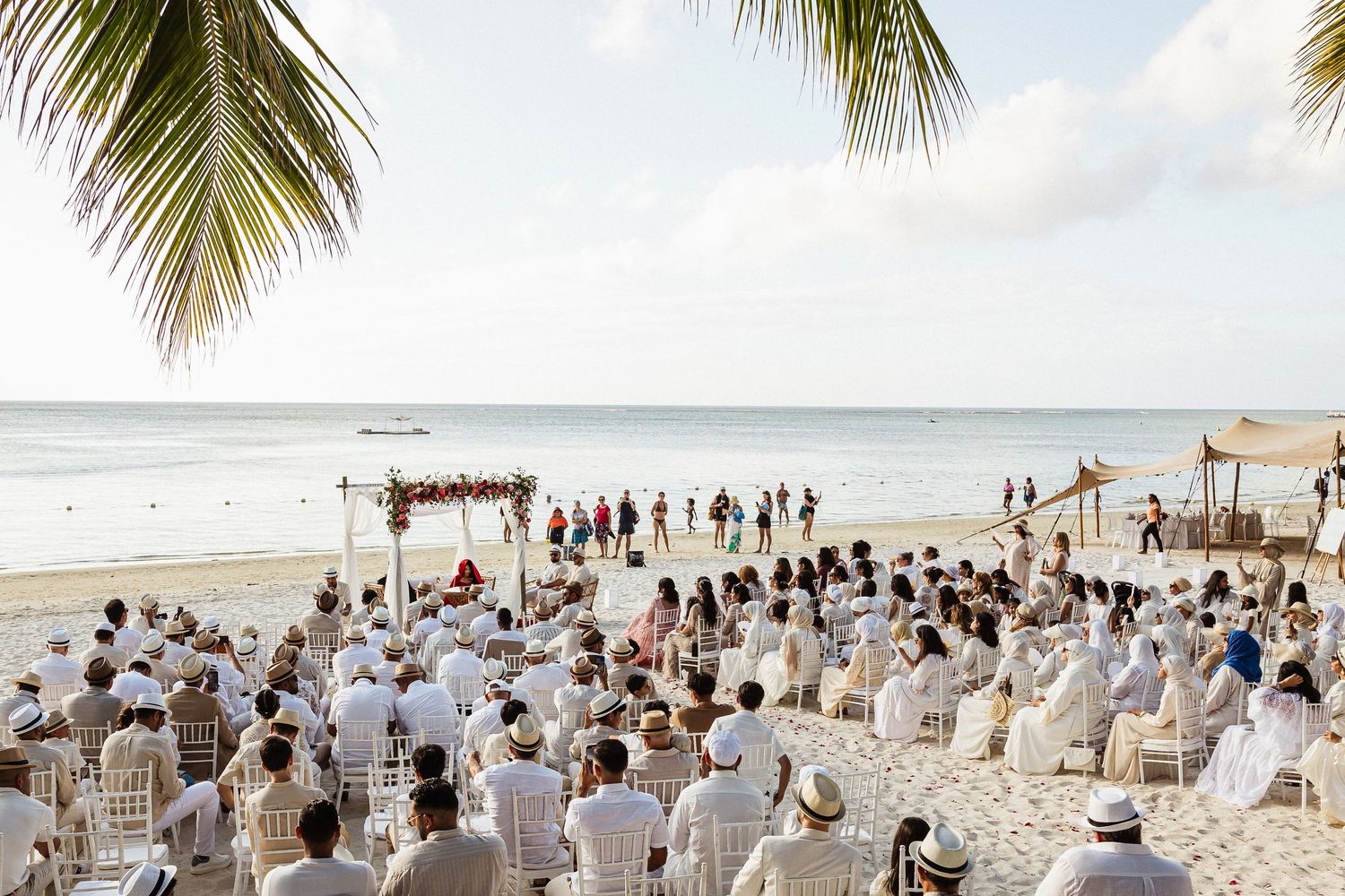 An elegant beach wedding ceremony setup with white chairs and tropical palm trees.