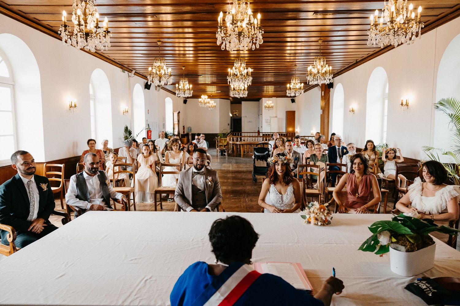 Wedding ceremony in an elegant hall with wooden ceiling and crystal chandeliers.