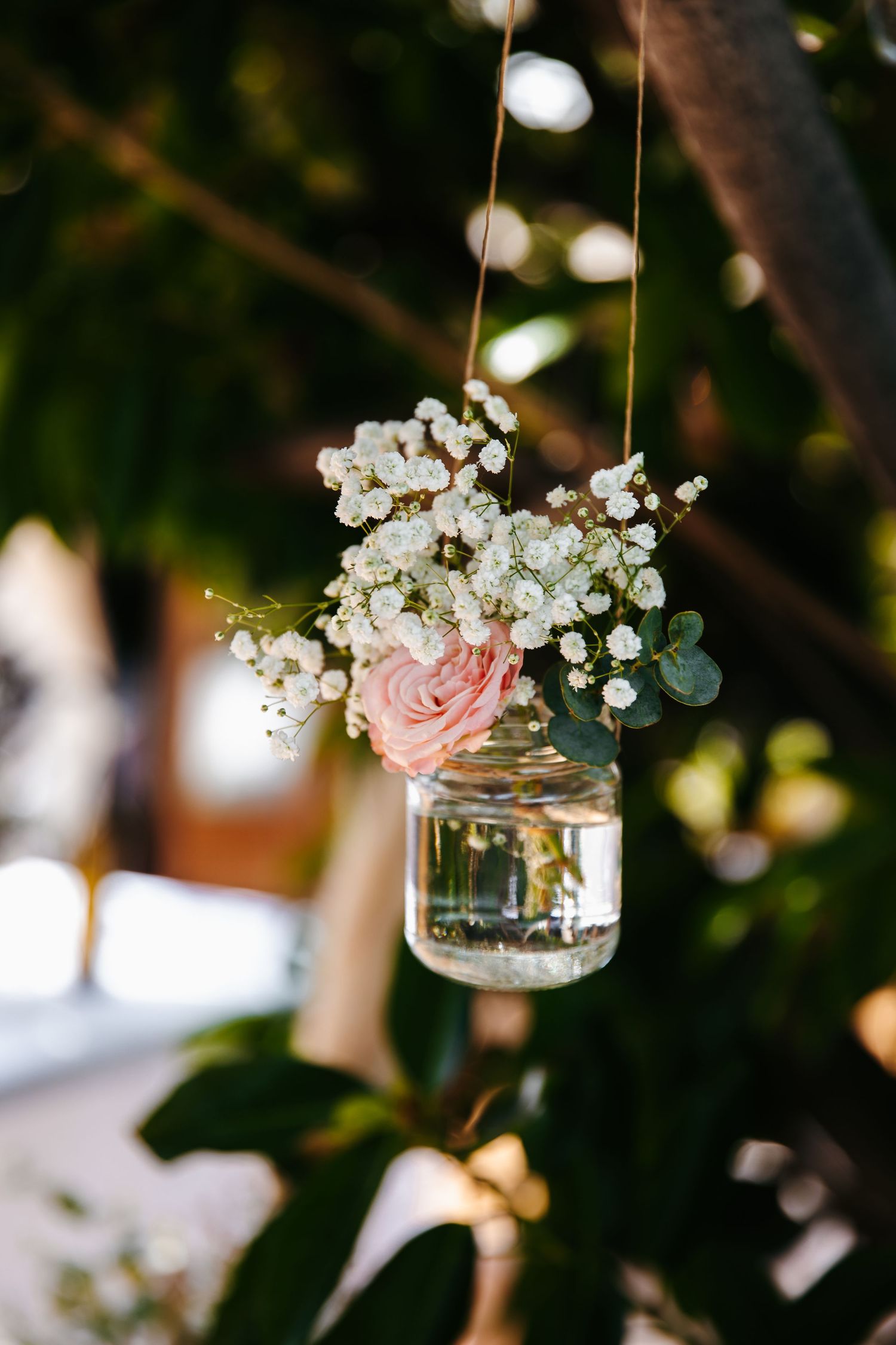 Mason jar with delicate pink rose and baby's breath flowers hanging as wedding decoration.