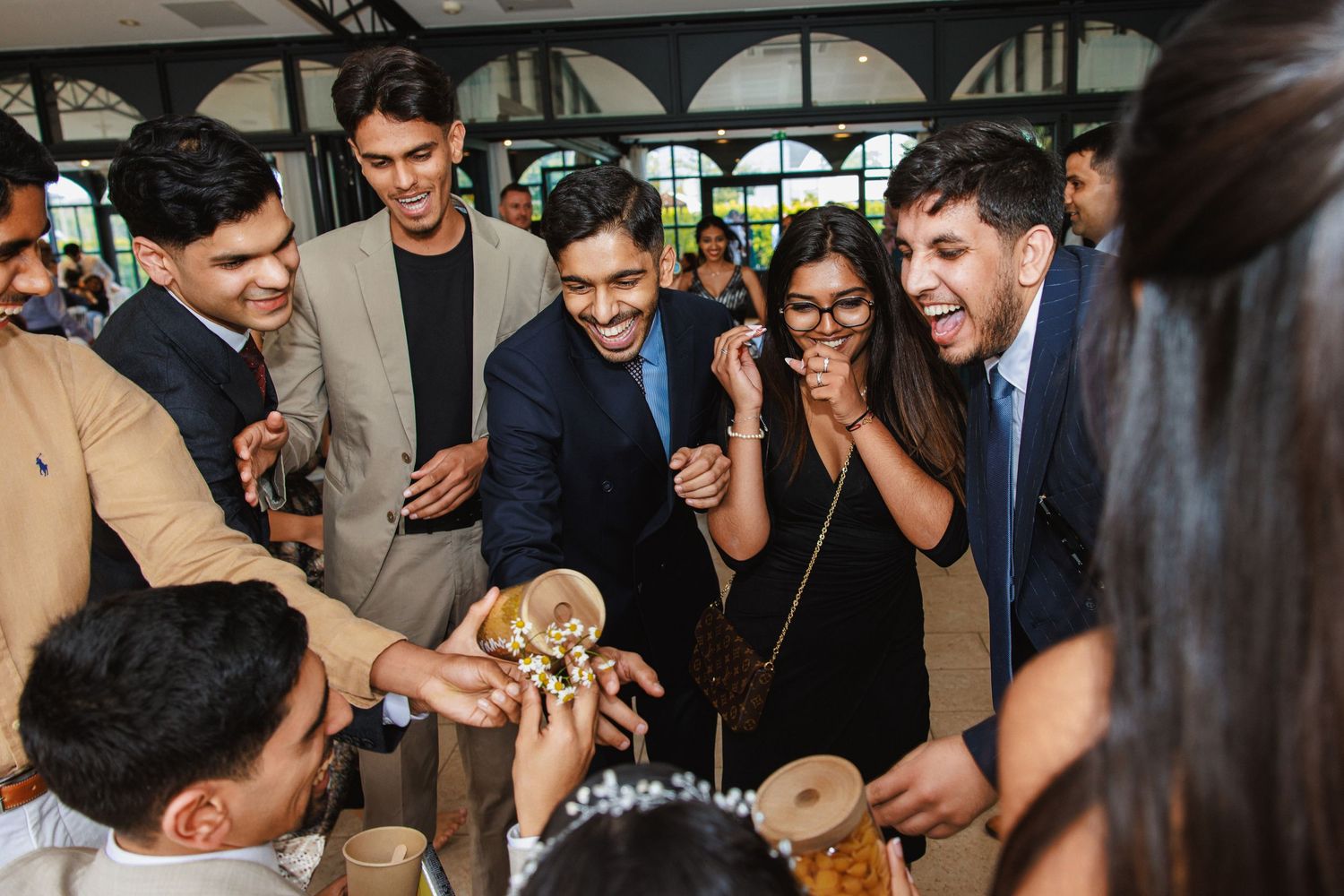 Wedding guests gather around excitedly looking at something being shown in the center of the group.