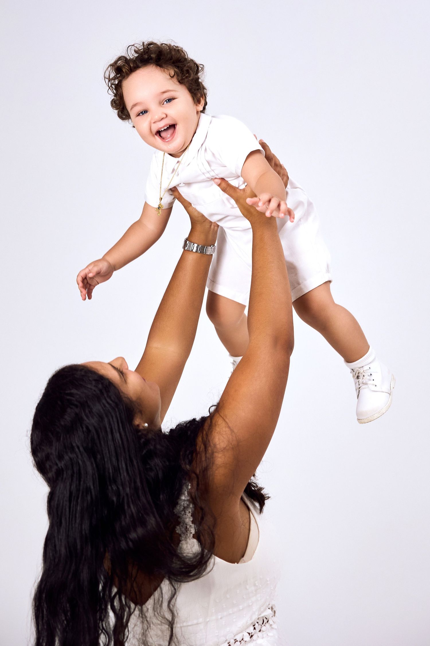 Playful photos of person lifting smiling baby wearing white in studio setting.