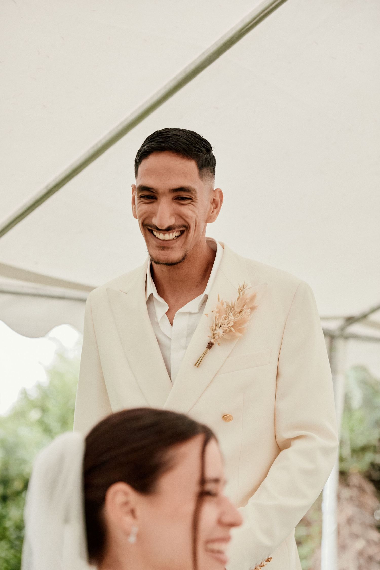 Candid wedding moment showing genuine laughter under a white tent.