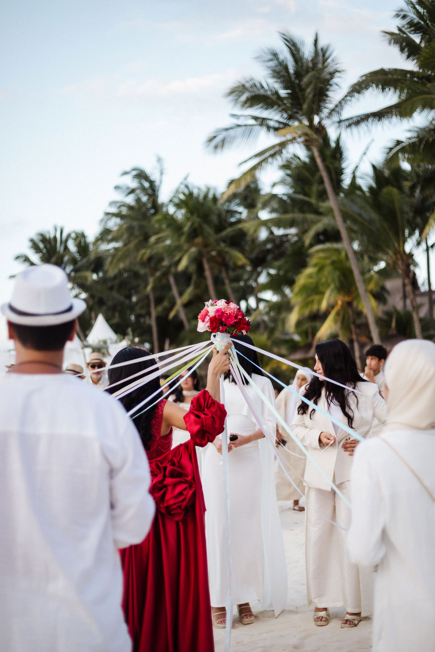 Wedding ceremony with guests in white creating arch for bride in red gown.