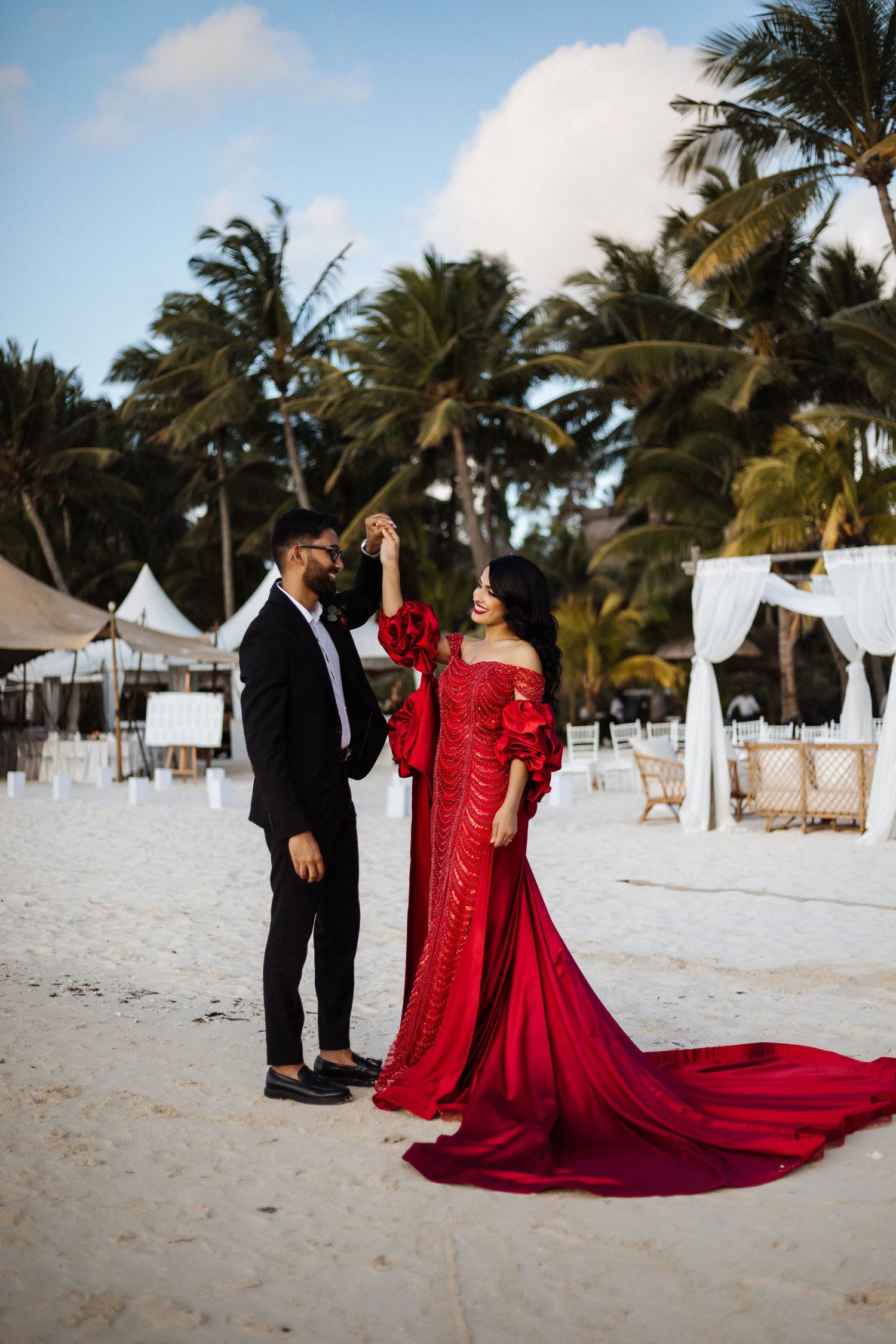 Tropical beach wedding scene with dramatic red wedding gown and palm trees.