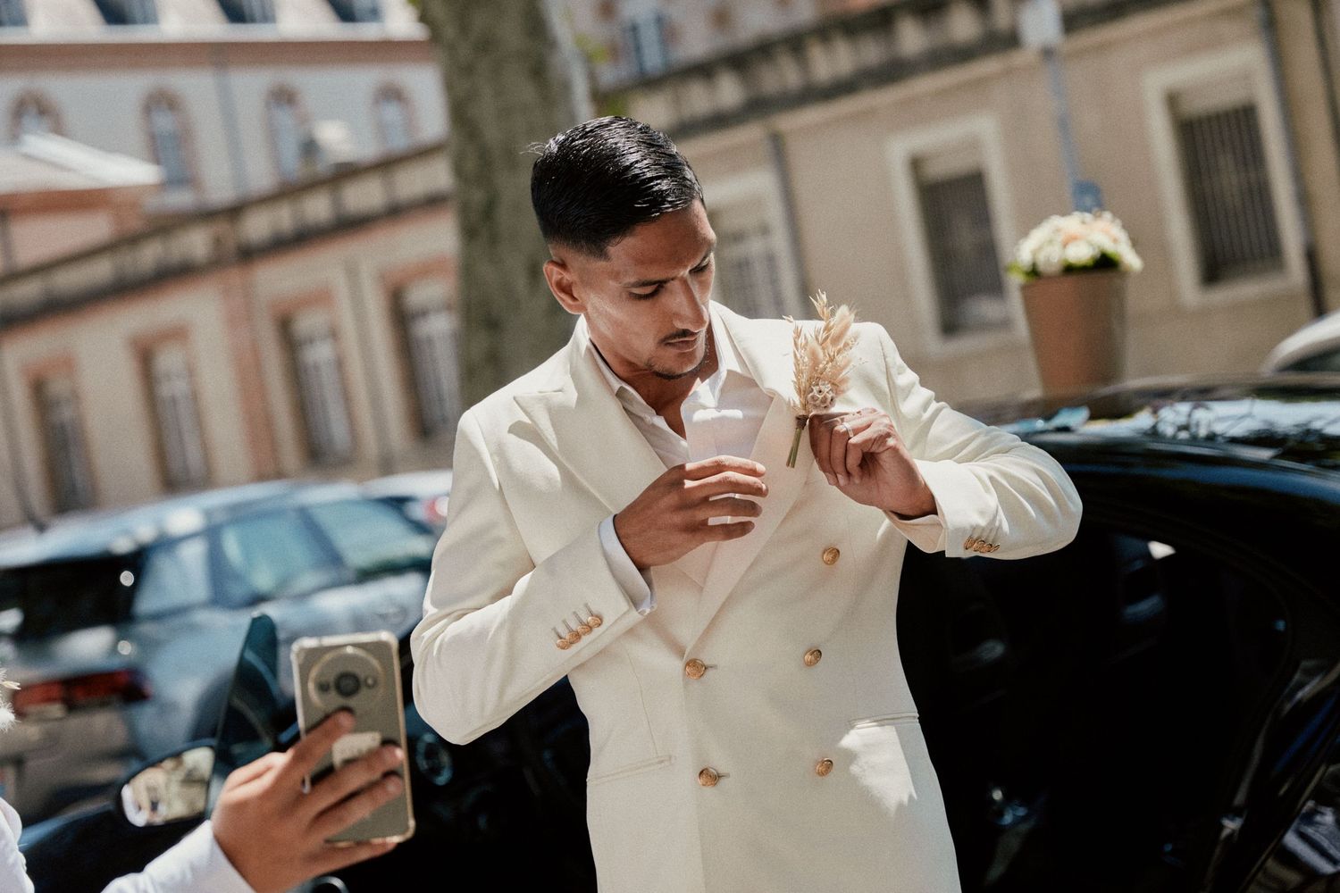 A person in a white suit jacket adjusting their tie while someone takes a photo.