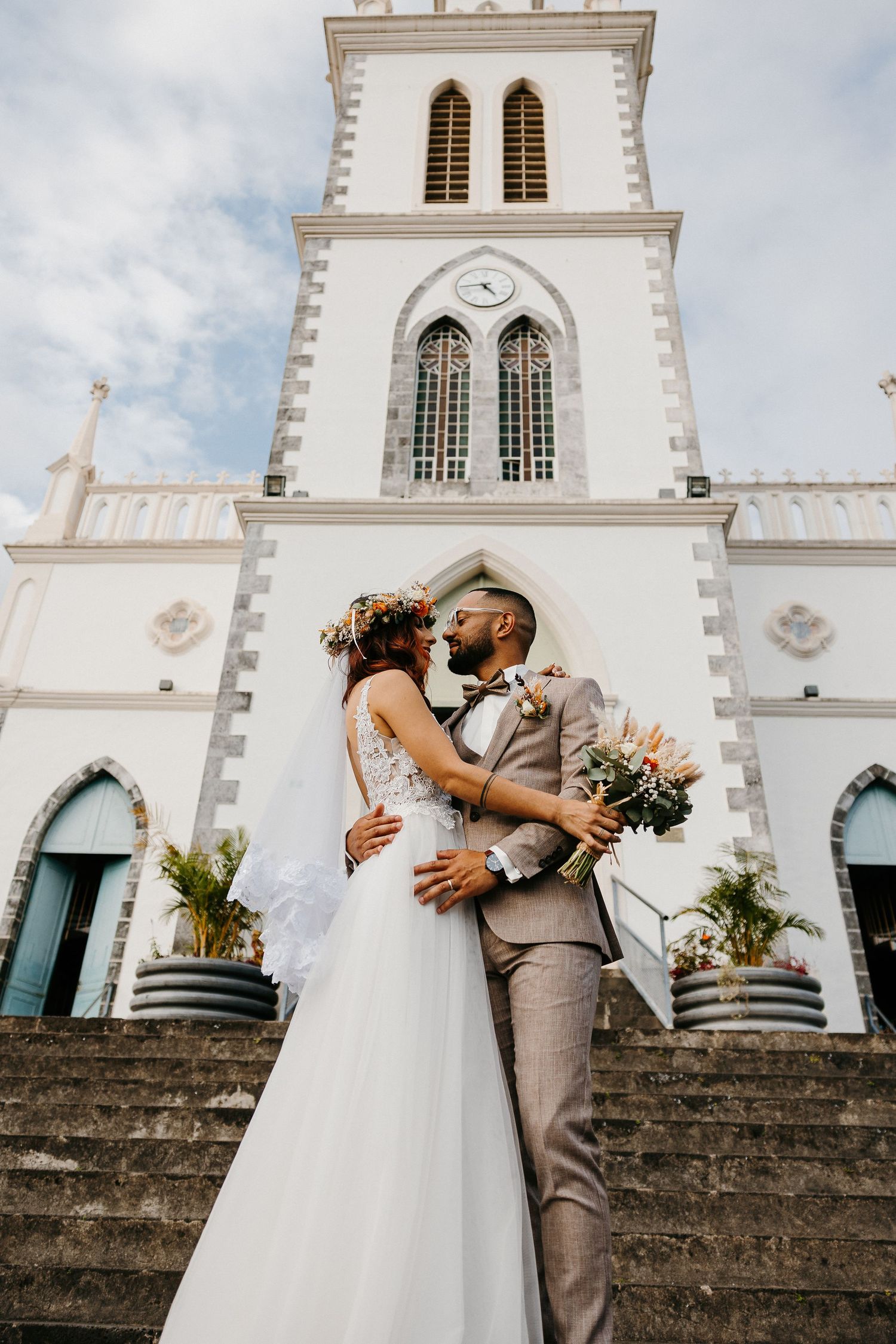 Romantic wedding portrait of couple embracing in front of white church tower.