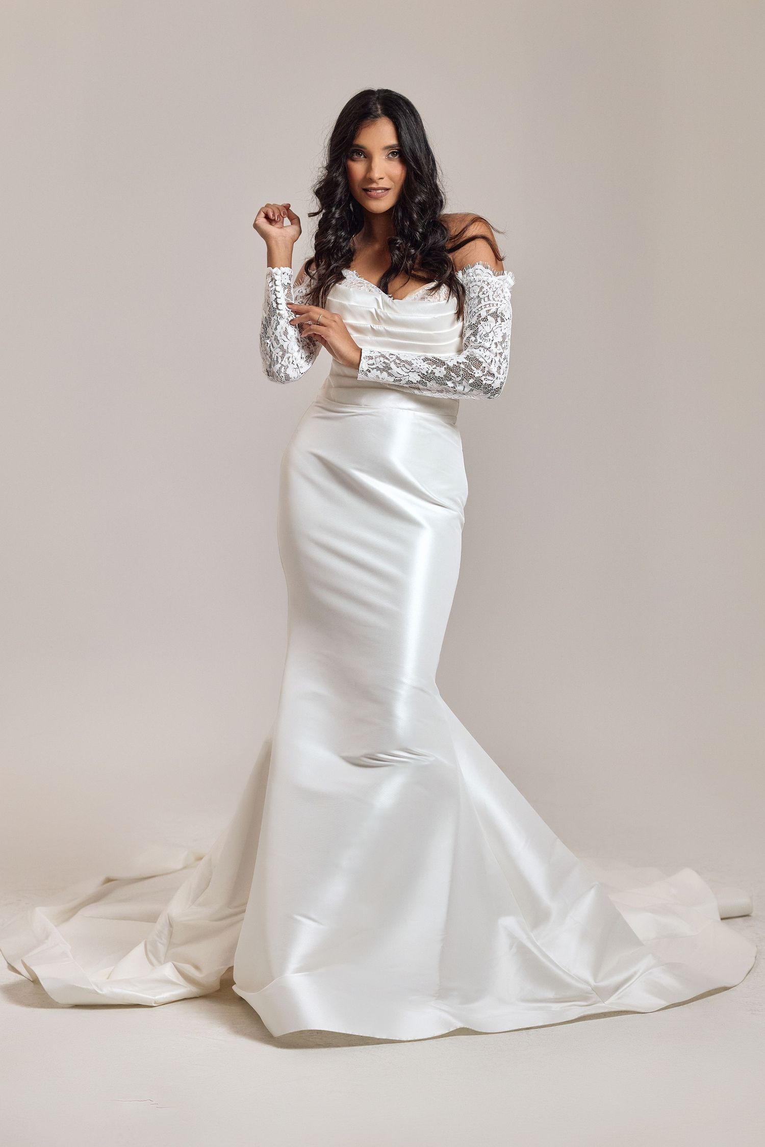 Woman in white bridal gown poses elegantly on beige background in studio photoshoot series.