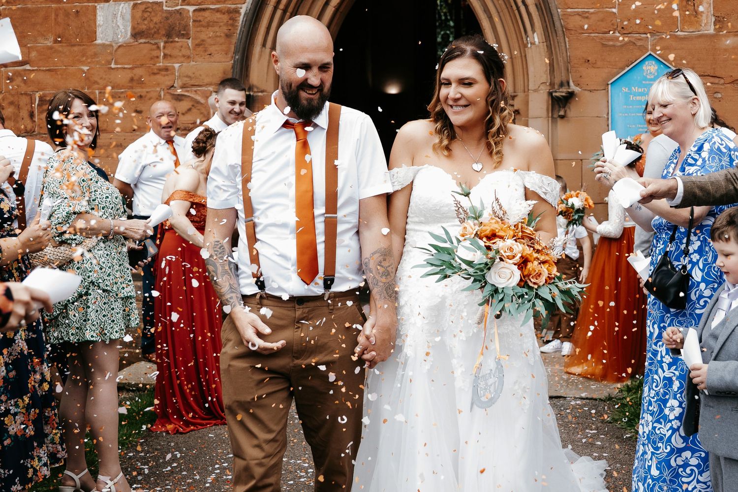 Wedding celebration outside church with guests throwing confetti at newlyweds.