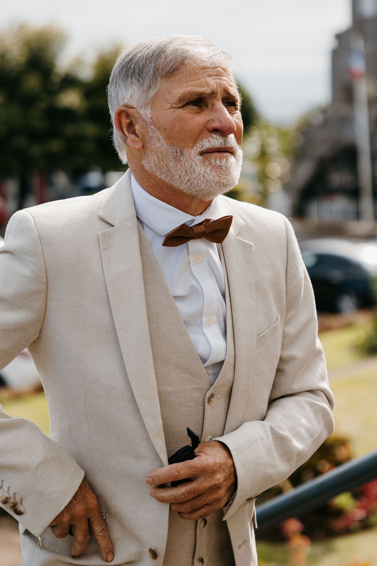 Elegant gentleman in beige suit and bowtie at outdoor wedding venue.