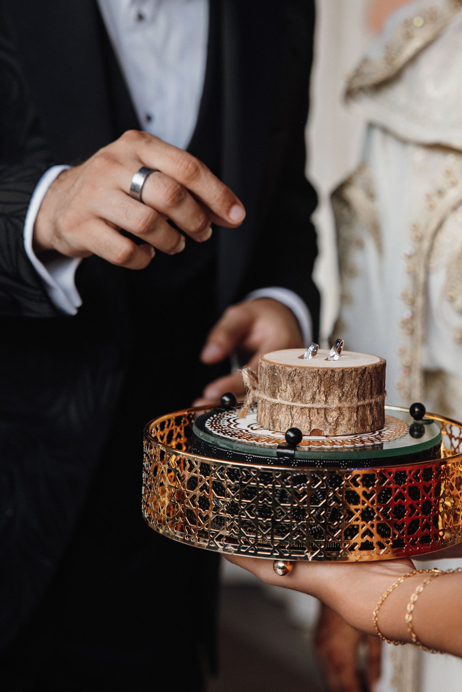 Close-up of hands presenting wedding rings on decorative metallic display holder.