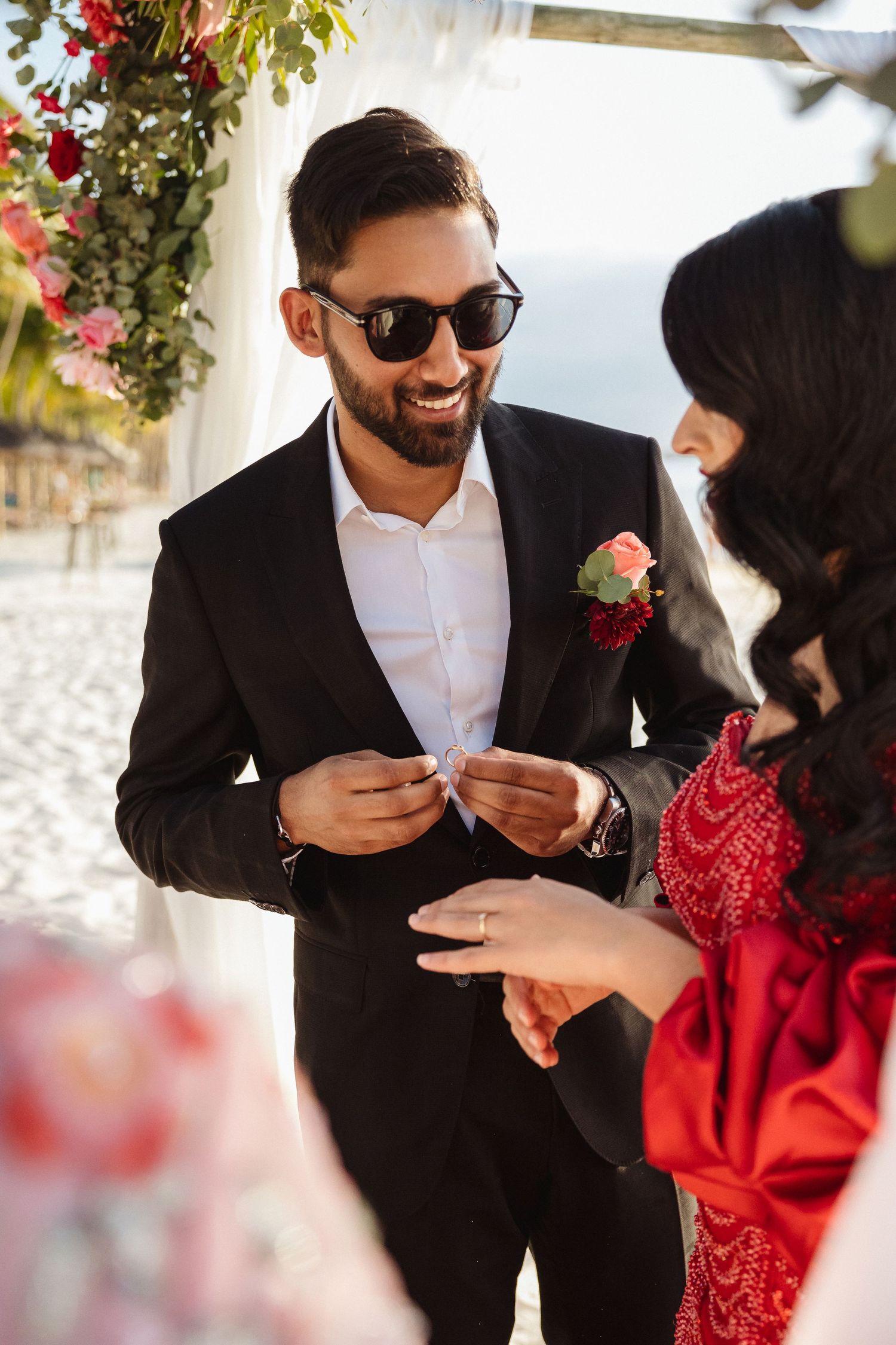 Couple exchanges rings during beach wedding ceremony under floral arch.