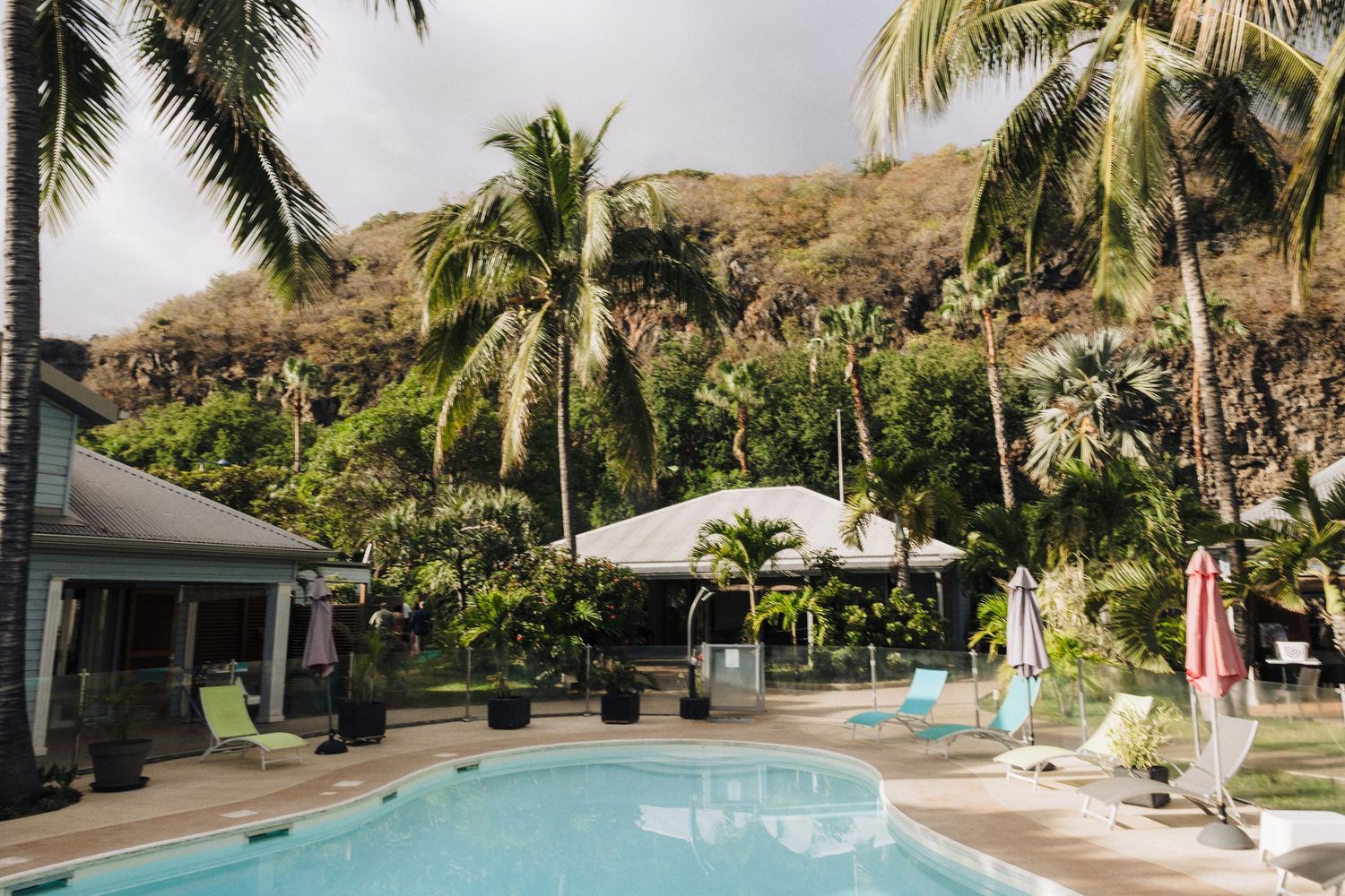 Luxury resort pool surrounded by palm trees and mountains with white umbrellas and lounge chairs.