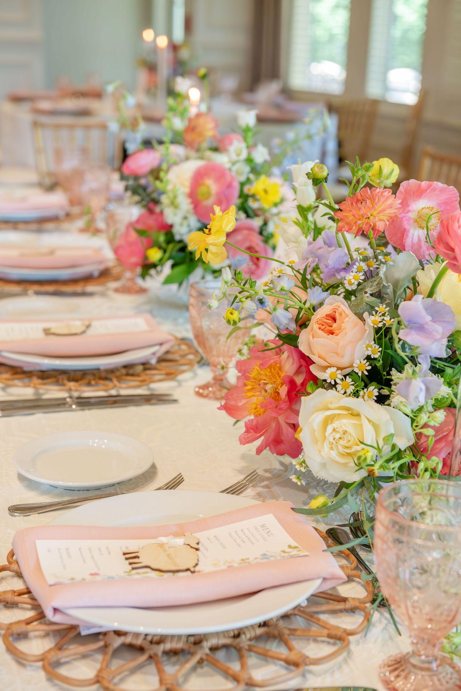 Elegant table setting with pink and yellow floral centerpieces, crystal glasses, and gold accents for a spring celebration.