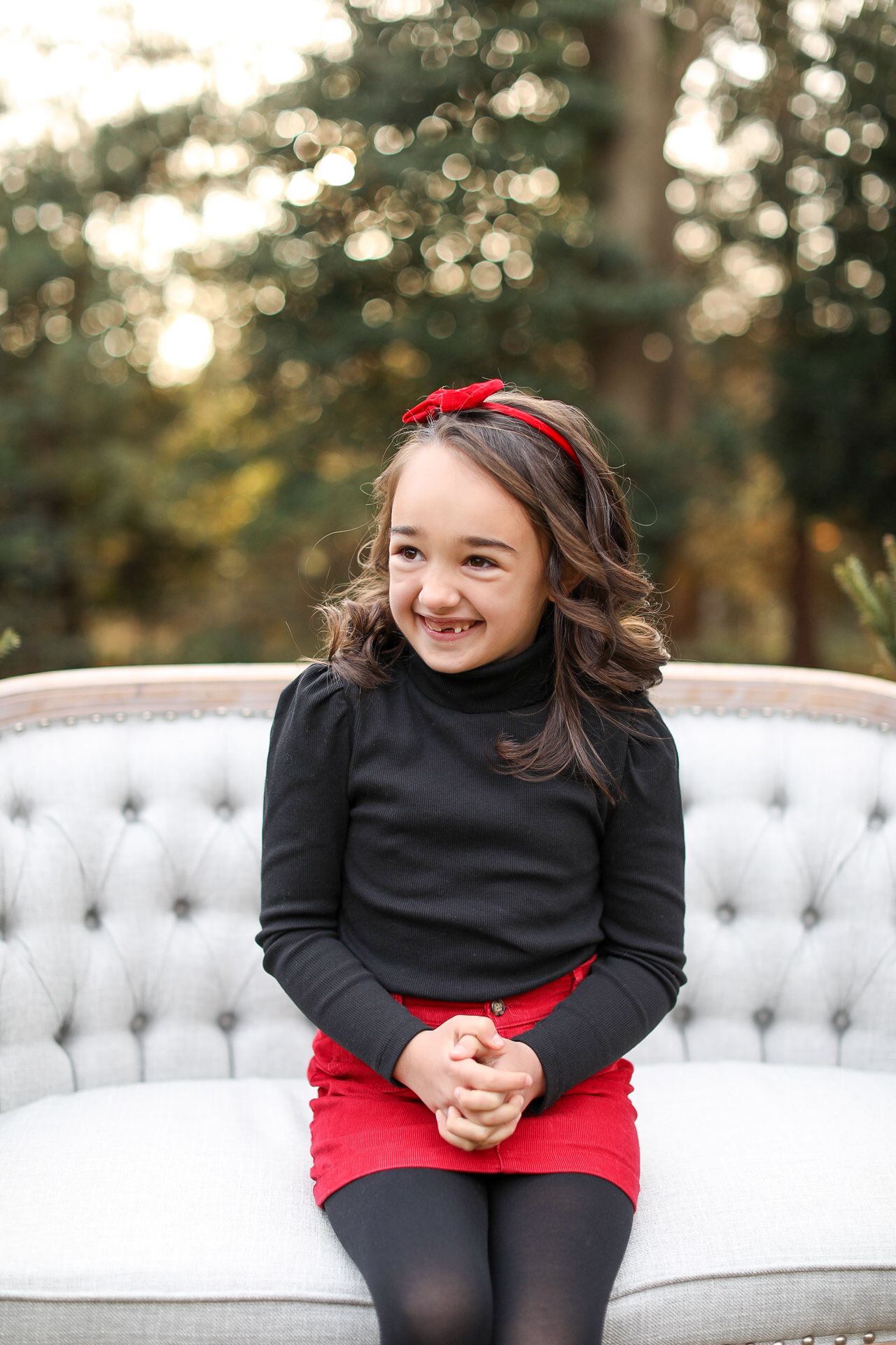 A person in black and red outfit sits and laughs joyfully on a white tufted couch outdoors at sunset.